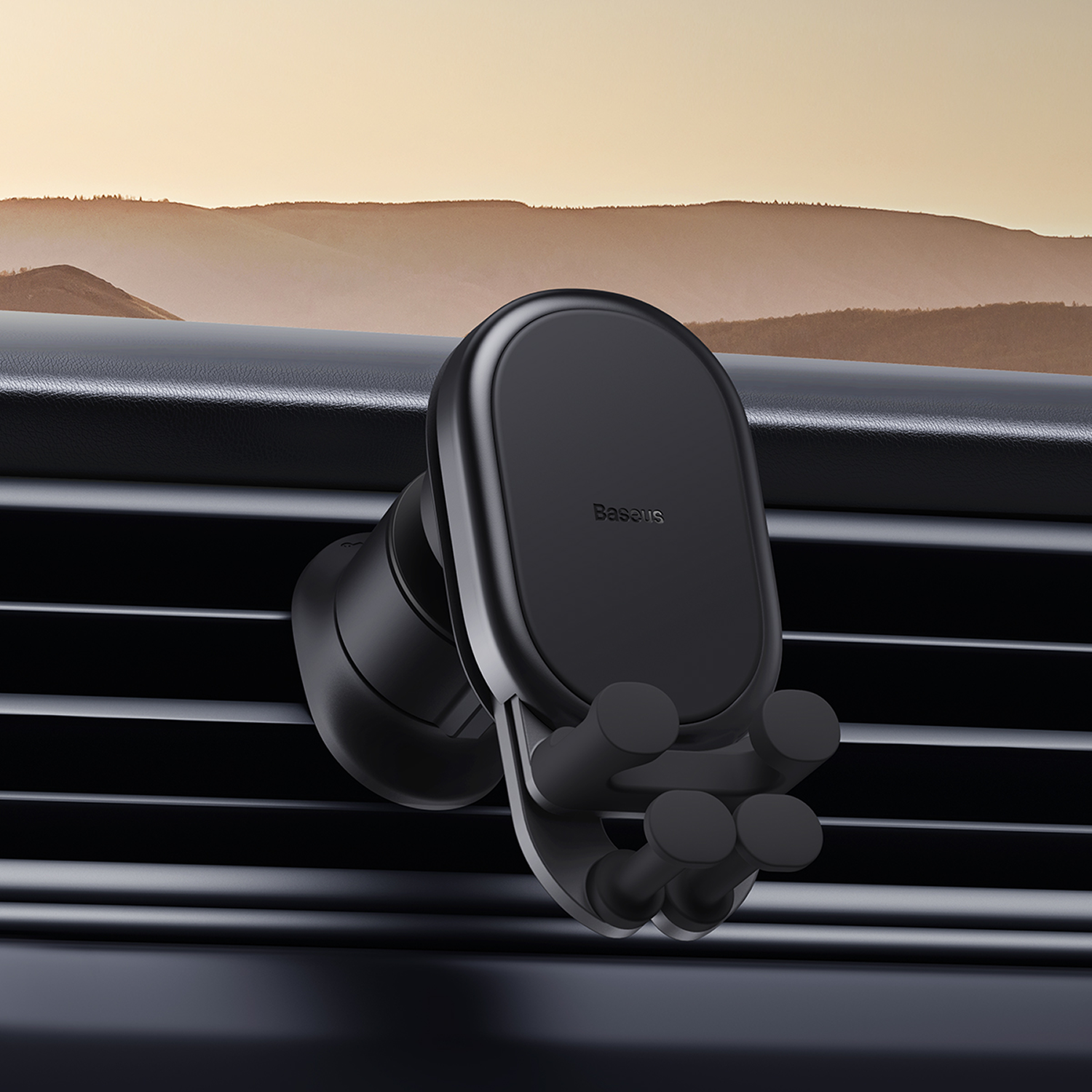 Soporte negro Baseus para teléfono de coche montado en una rejilla de ventilación. El fondo muestra una puesta de sol sobre montañas.