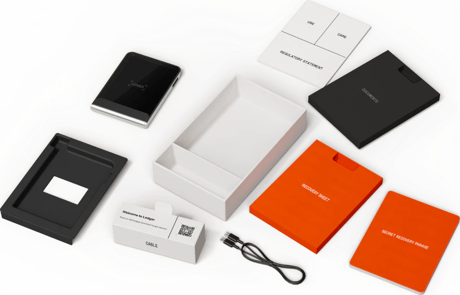Ledger Hardware-Wallet-Kit mit Zubehör: schwarzes Gerät, weiße Box, orangefarbene Recovery-Sheets und Kabel.