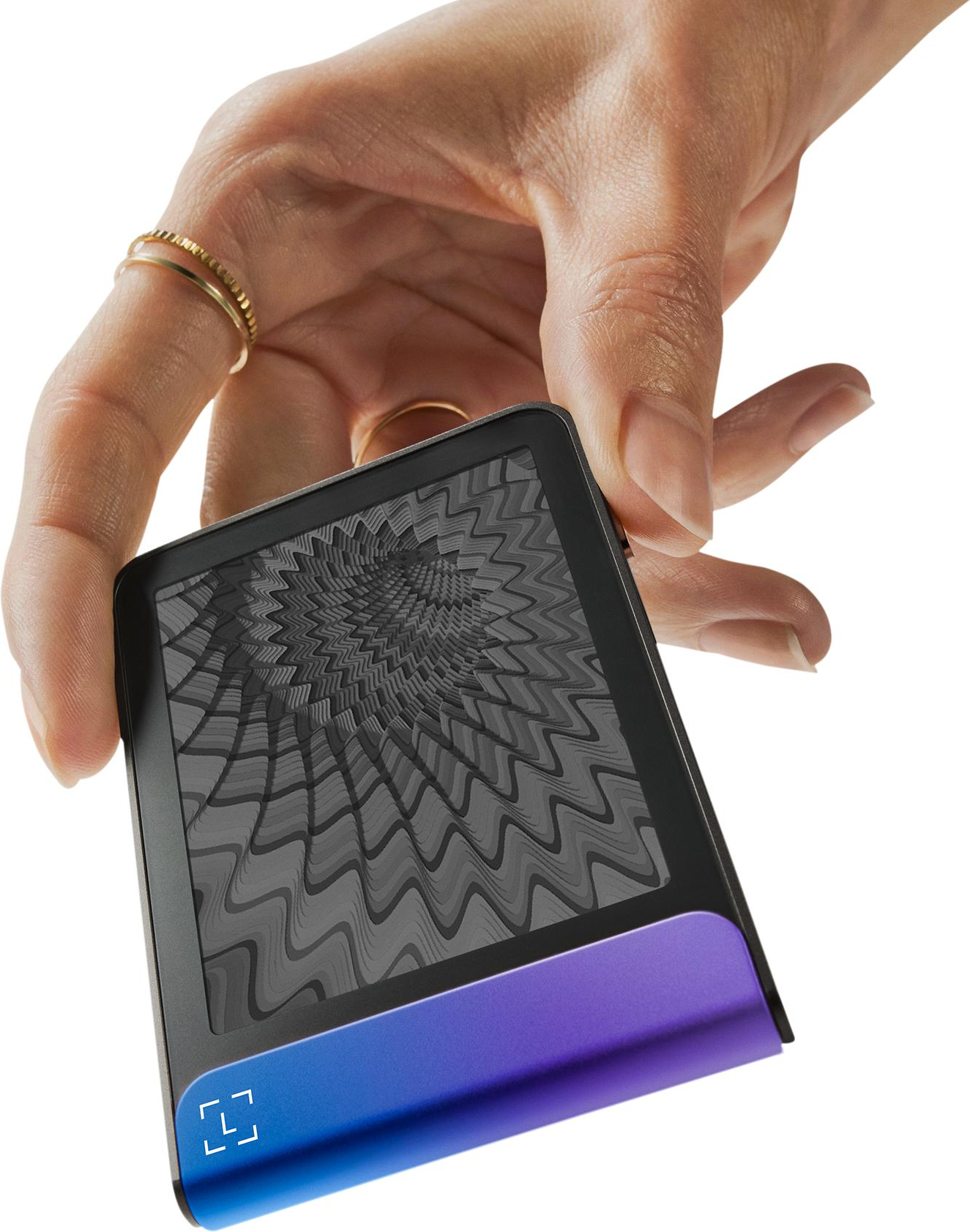 Mano che tiene in mano un dispositivo con schermo a motivi. Anelli adornano le dita. Il dispositivo ha una base sfumata viola e blu.
