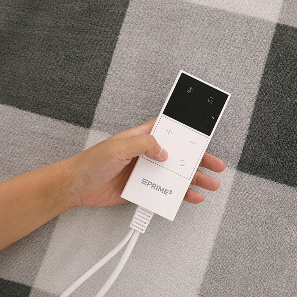 Dłoń trzyma biały pilot PRIME3. Pilot ma przyciski i czarny ekran. Biały kabel wychodzi z dołu.