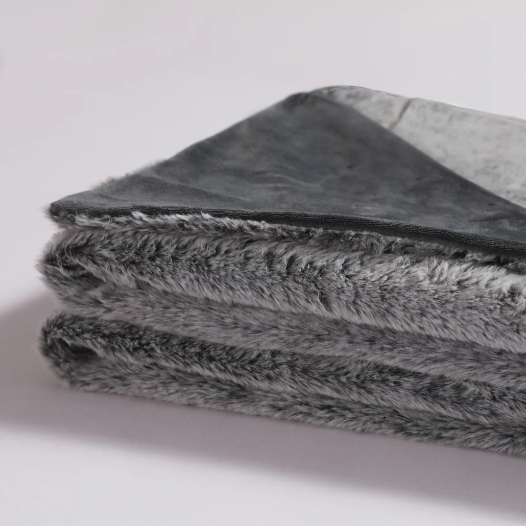 Złożony szary koc z pluszową, futerkową fakturą. Górna warstwa jest gładka, ciemnoszara. Tło jest gładkie białe.