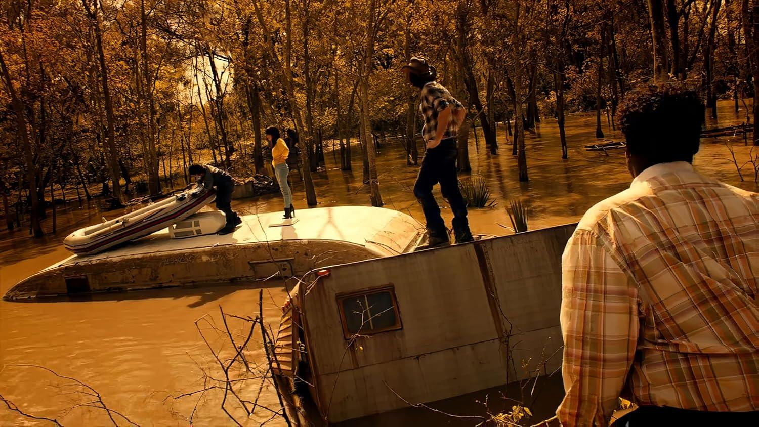 Menschen stehen auf überfluteten Strukturen, mit einem Boot. Bäume sind im Hintergrund. Das Wasser ist braun.
