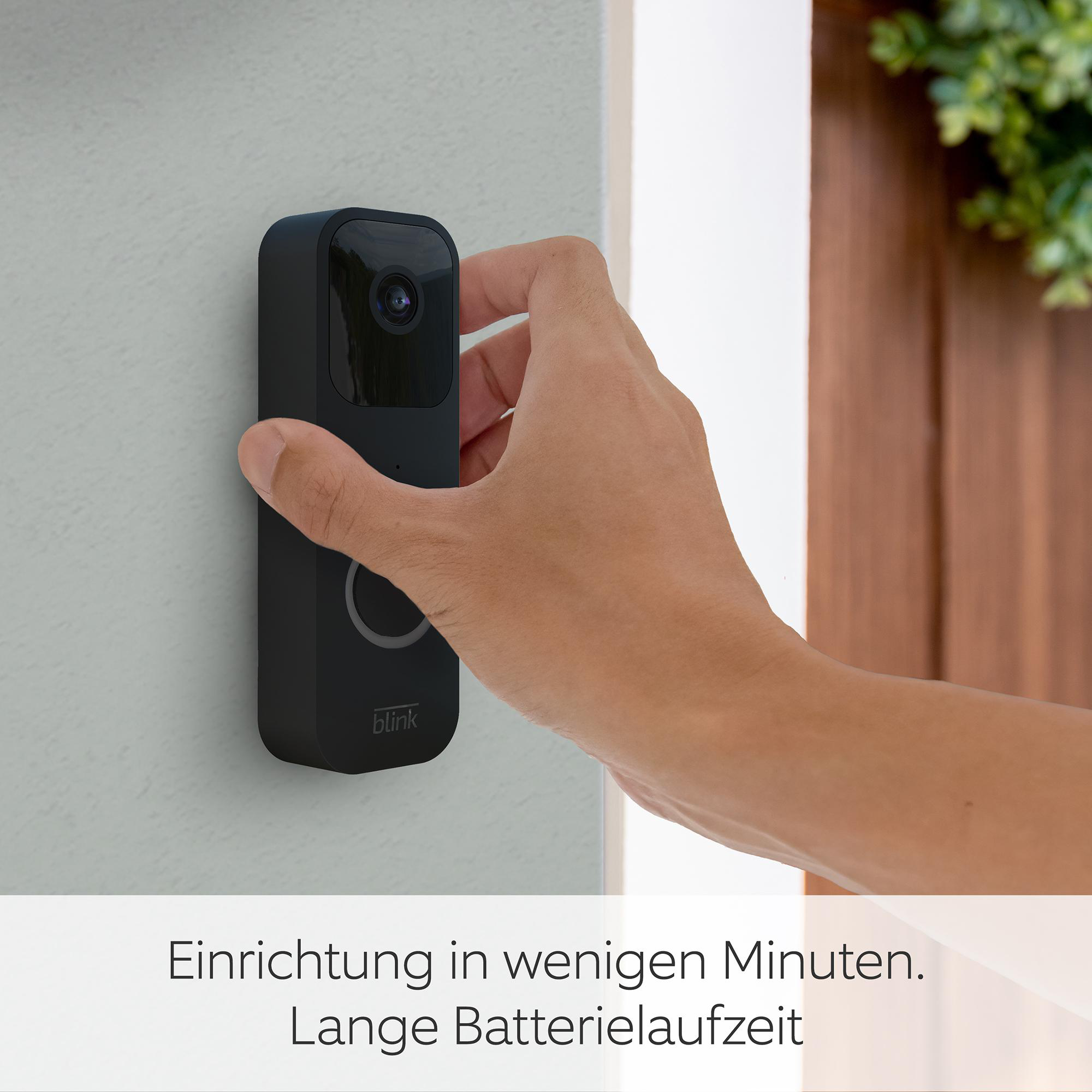 Eine Hand hält eine schwarze Blink-Video-Türklingel an einer grauen Wand. Text unten: Einrichtung in Minuten, lange Akkulaufzeit.