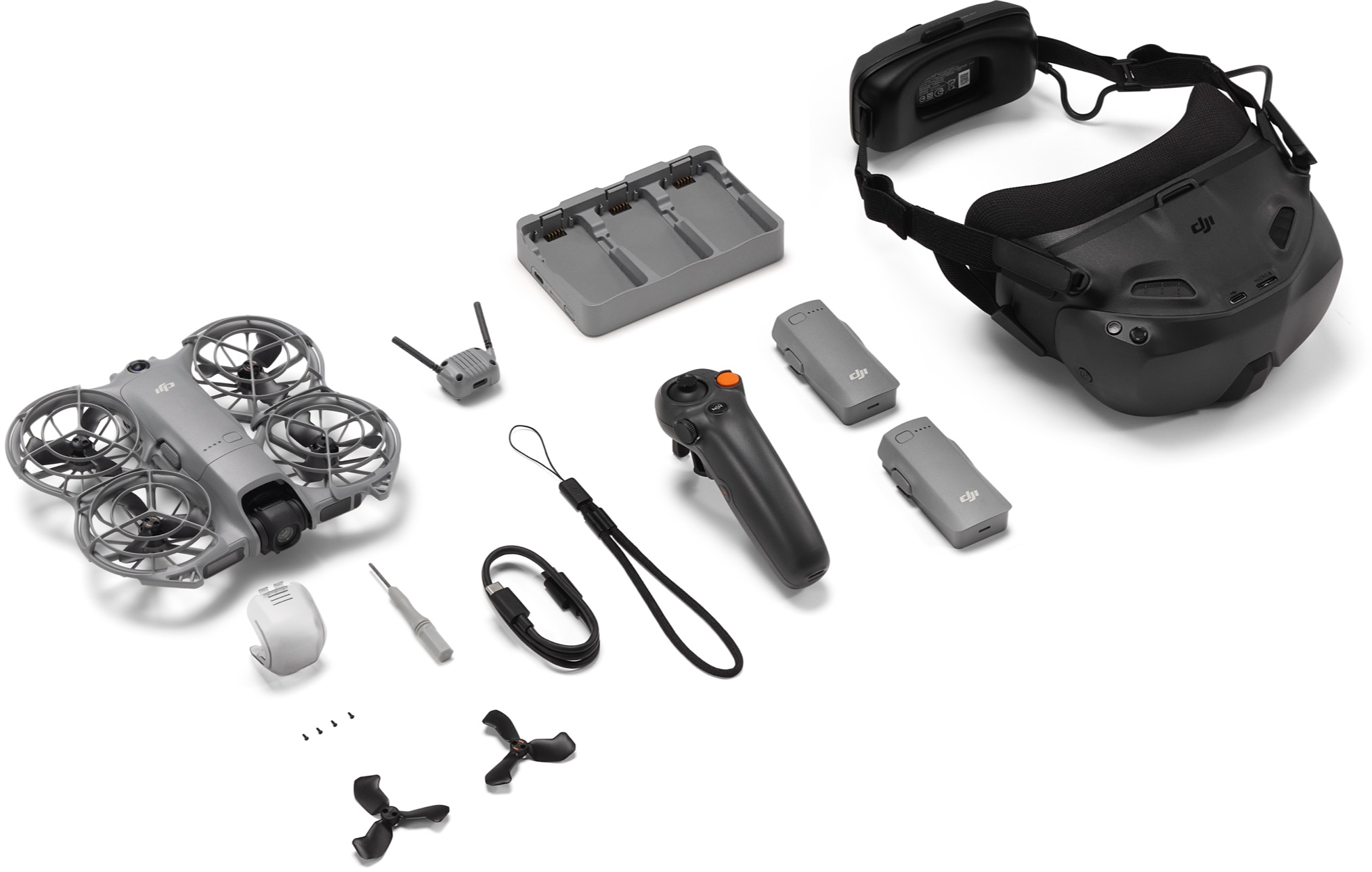 Drohnen-Kit mit Drohne, Controller, Brille, Batterien, Ladegerät und Zubehör auf weißer Oberfläche.