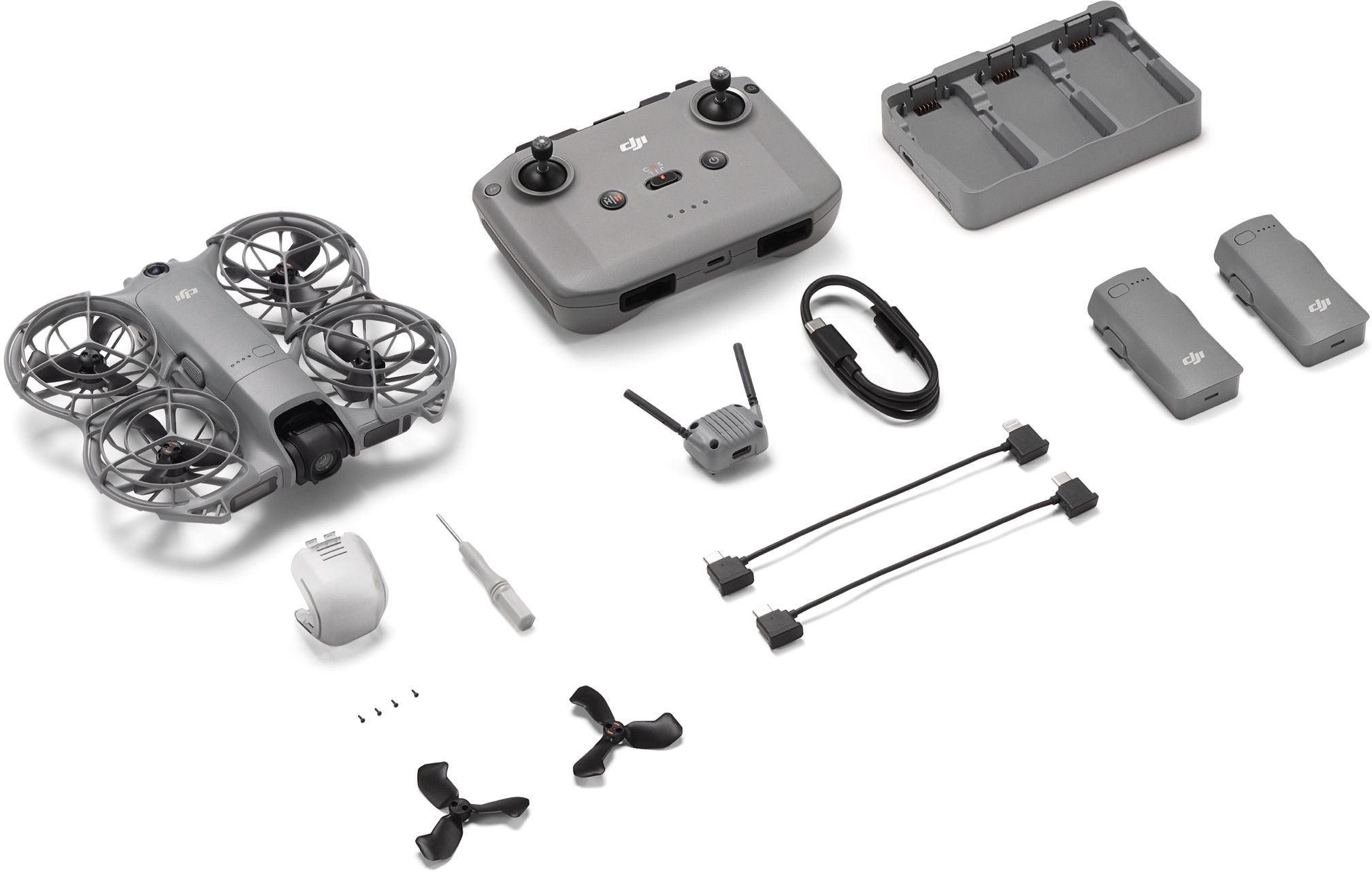 Eine graue Drohne mit Propellern, Controller, Batterien, Ladegerät, Kabeln und Zubehör ist auf einer weißen Oberfläche angeordnet.