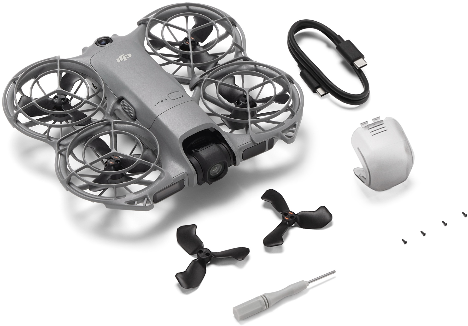 Un drone gris avec cage de protection, hélices noires, câble USB, cache de protection, vis et tournevis sur surface blanche.