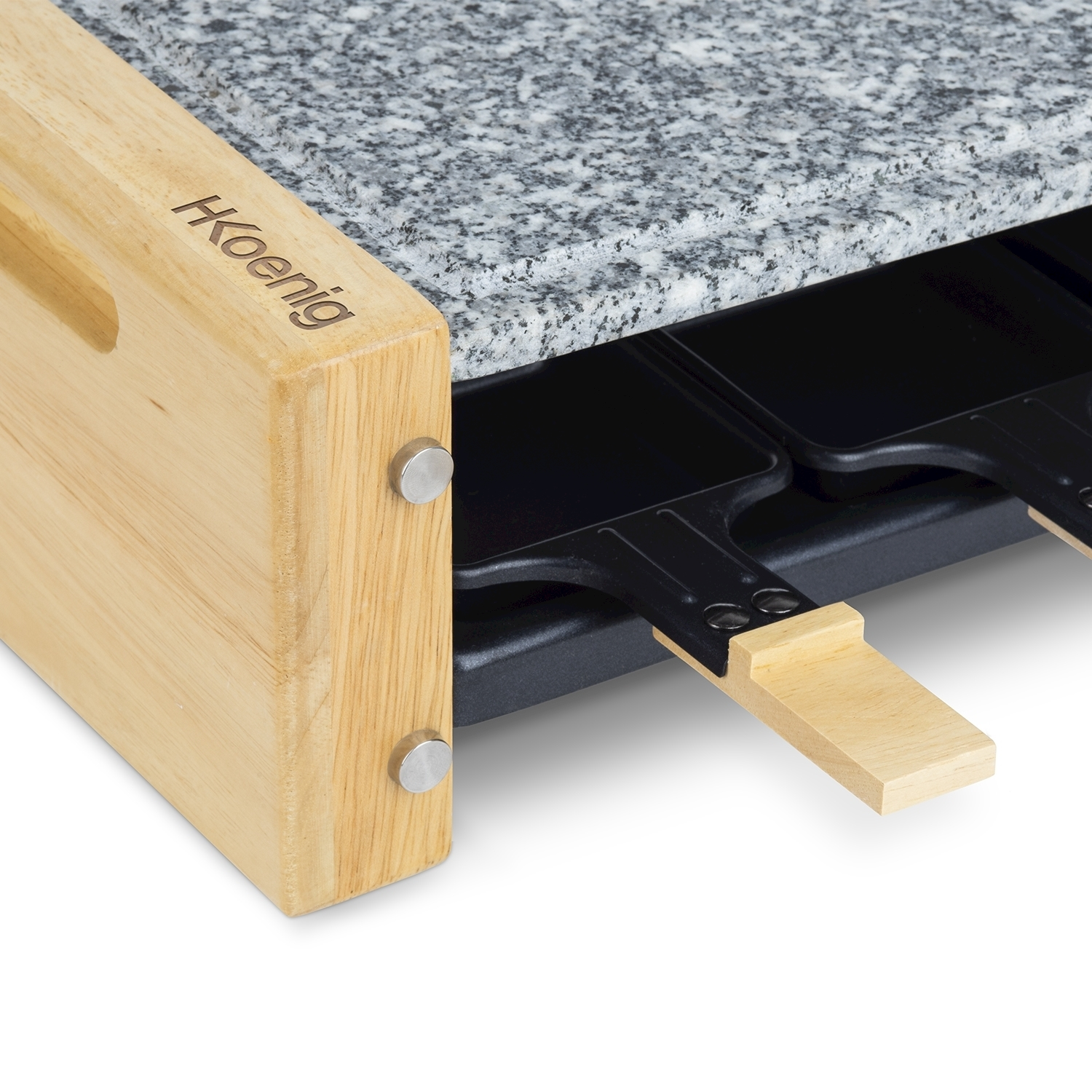 Primo piano di una griglia per raclette. Cornice in legno a sinistra, piano in granito, padelle nere sotto. Marchio 'Koenig' sul legno.