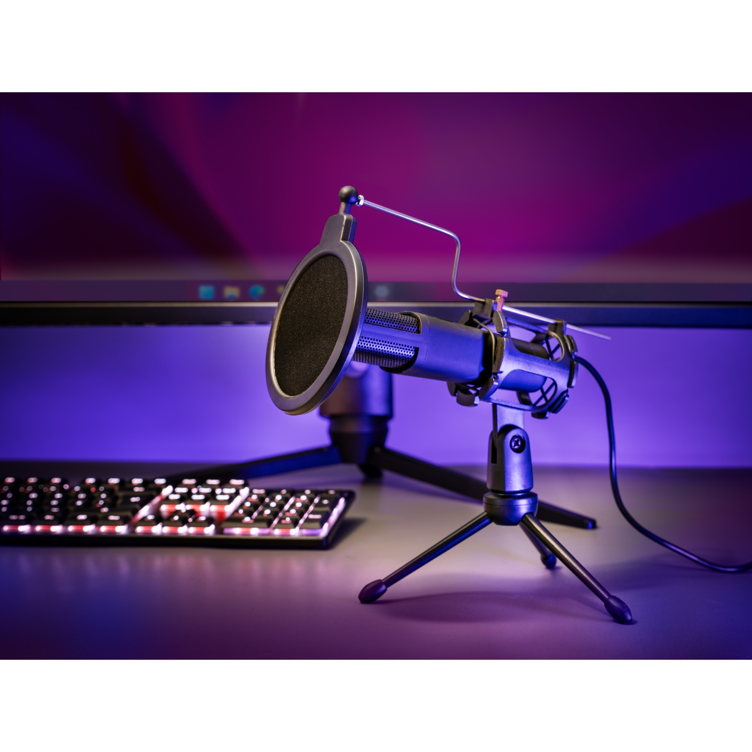 Un microfono con filtro antipop è su un treppiede. Una tastiera e un monitor sono sullo sfondo. La scena è illuminata con luce viola.