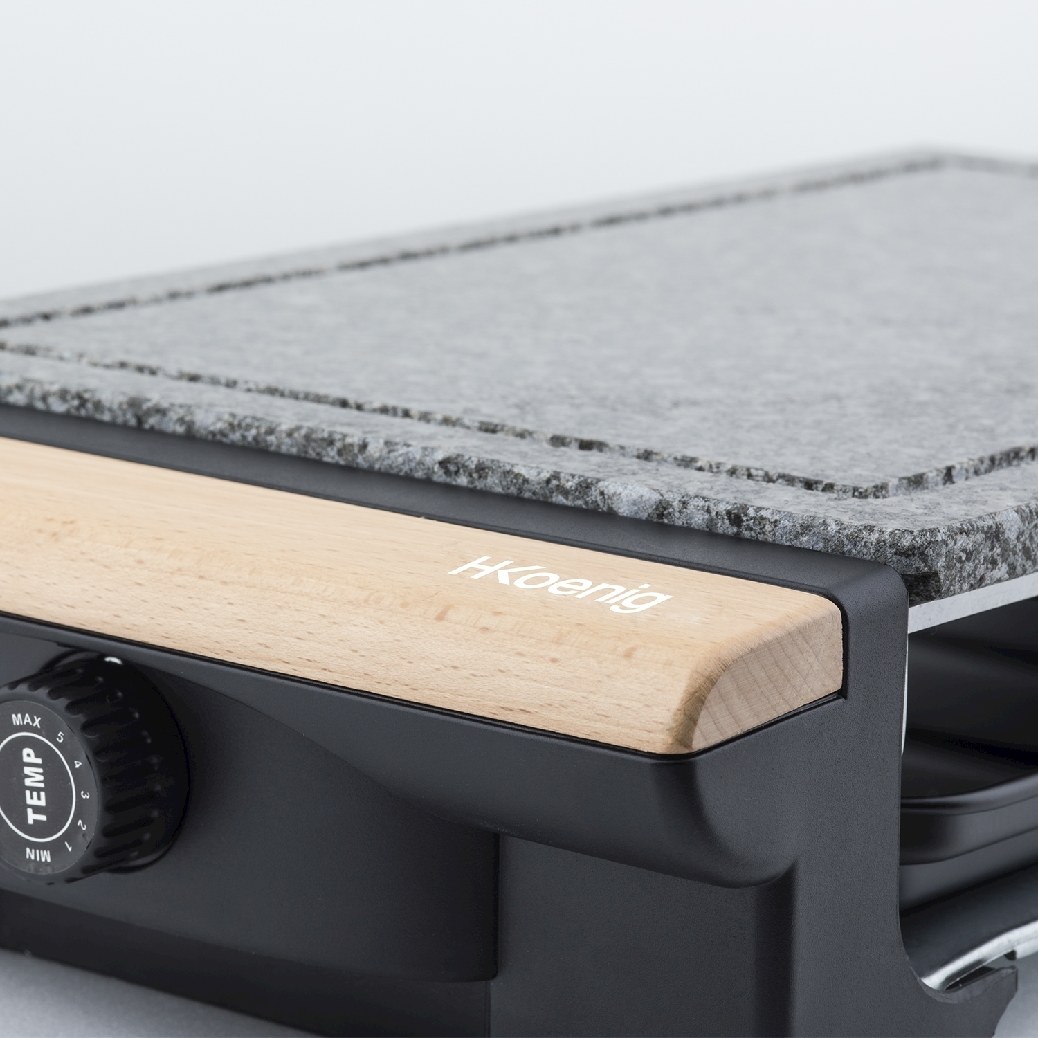 Primo piano di una griglia per raclette. Ha un piano in pietra, un manico in legno e una manopola per il controllo della temperatura. Il marchio è visibile.