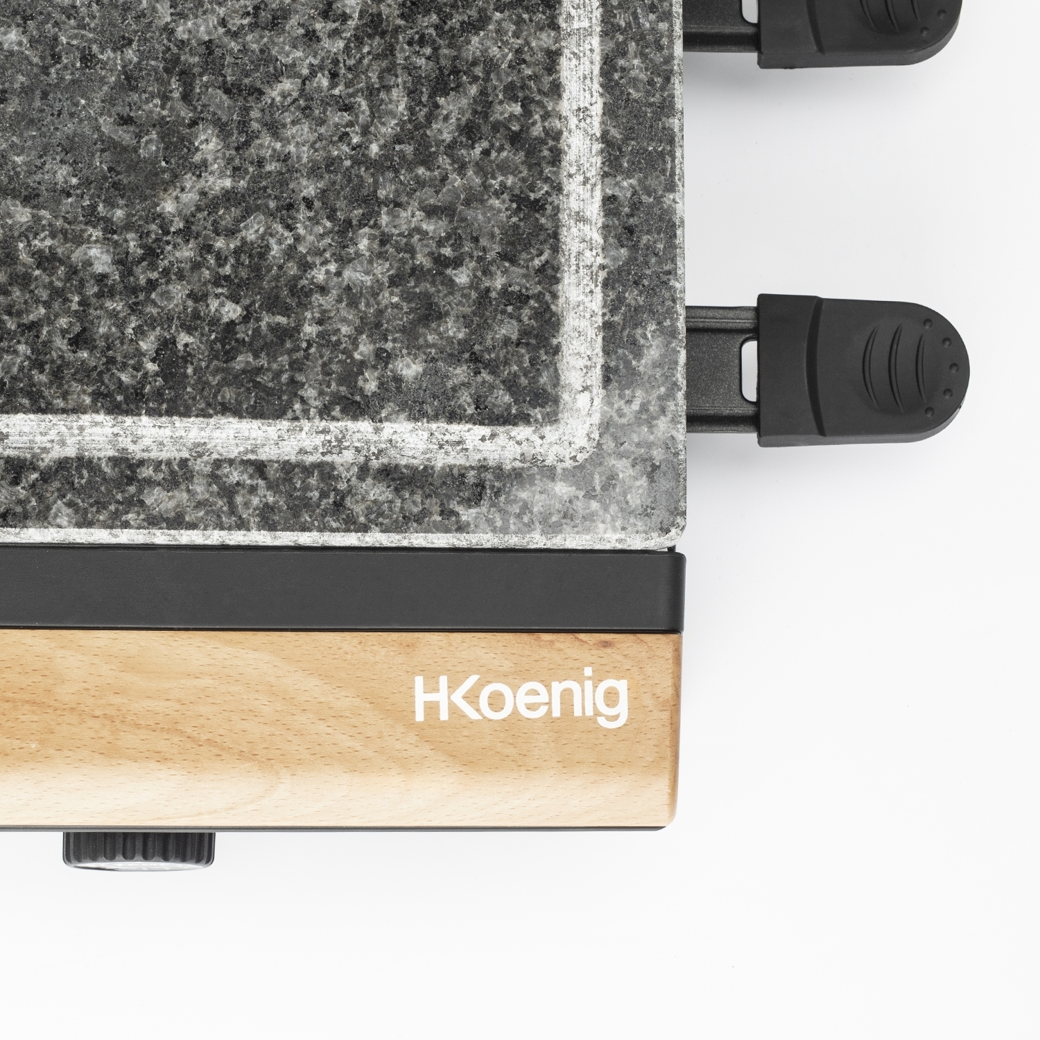 Primo piano di una griglia per raclette. Superficie in granito, manici e telaio neri, base in legno con logo 'HKoenig', su sfondo bianco.