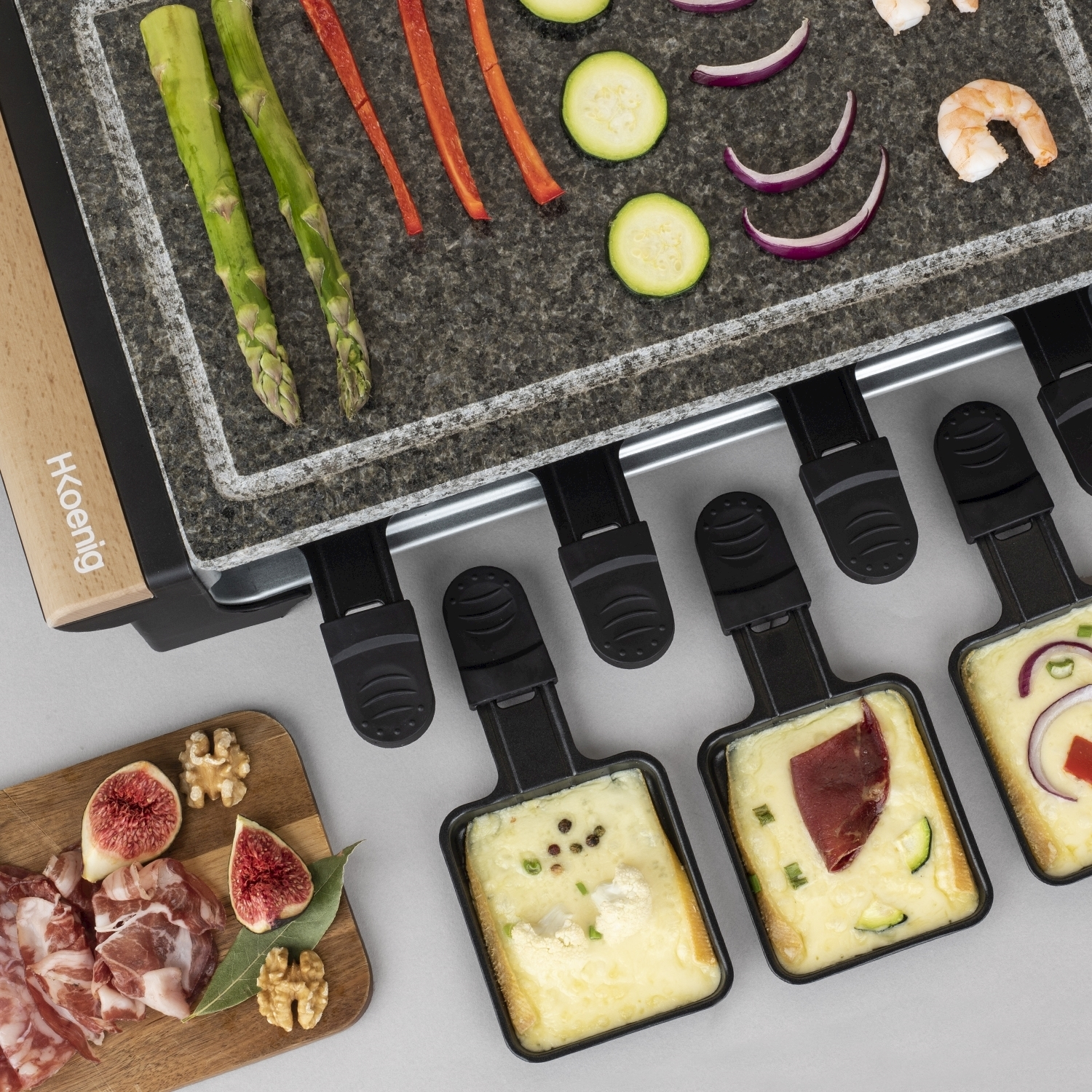 Grill per raclette con verdure e gamberi. Formaggio in padella, fichi, noci e salumi su un tagliere di legno.