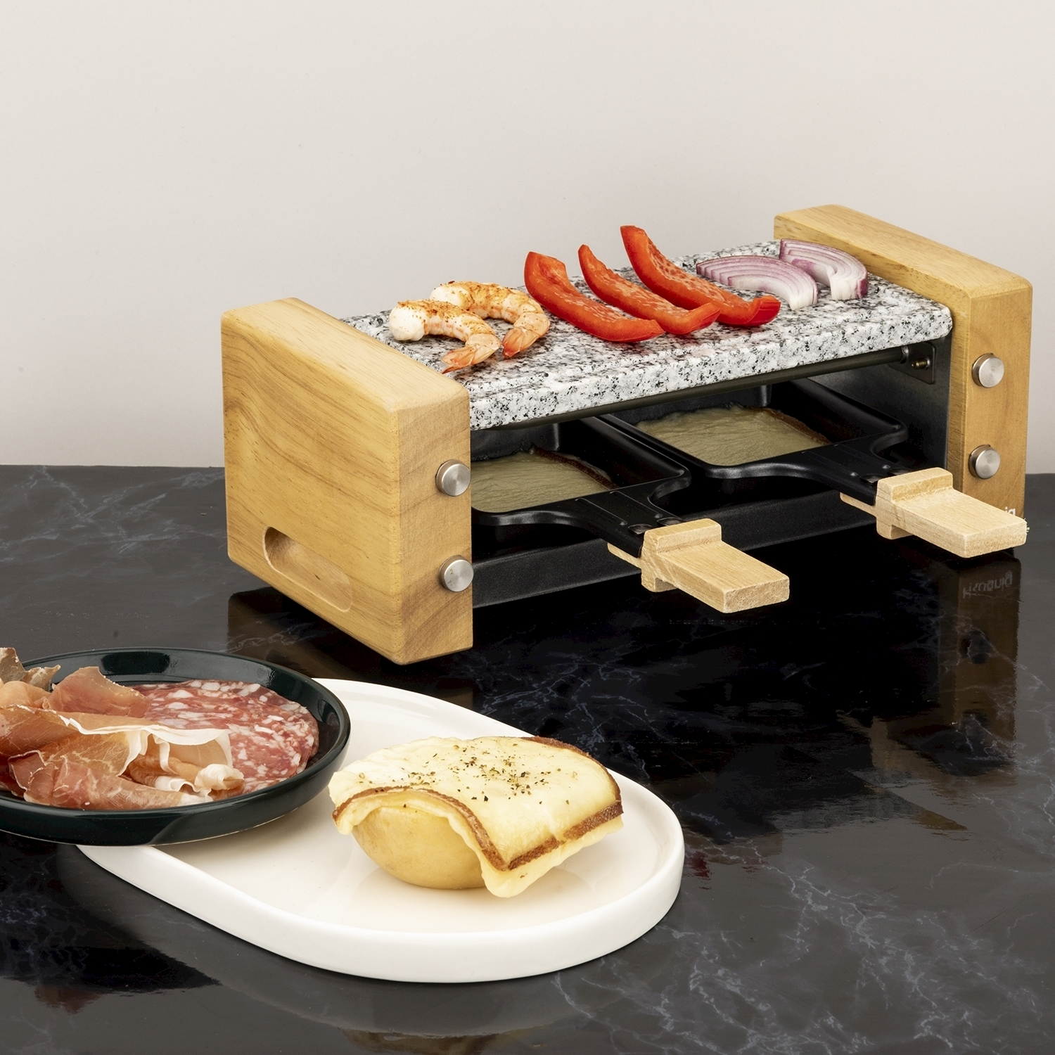 Griglia per raclette con gamberi, peperoni e cipolle. Salame e formaggio su piatti. Superficie in marmo nero.