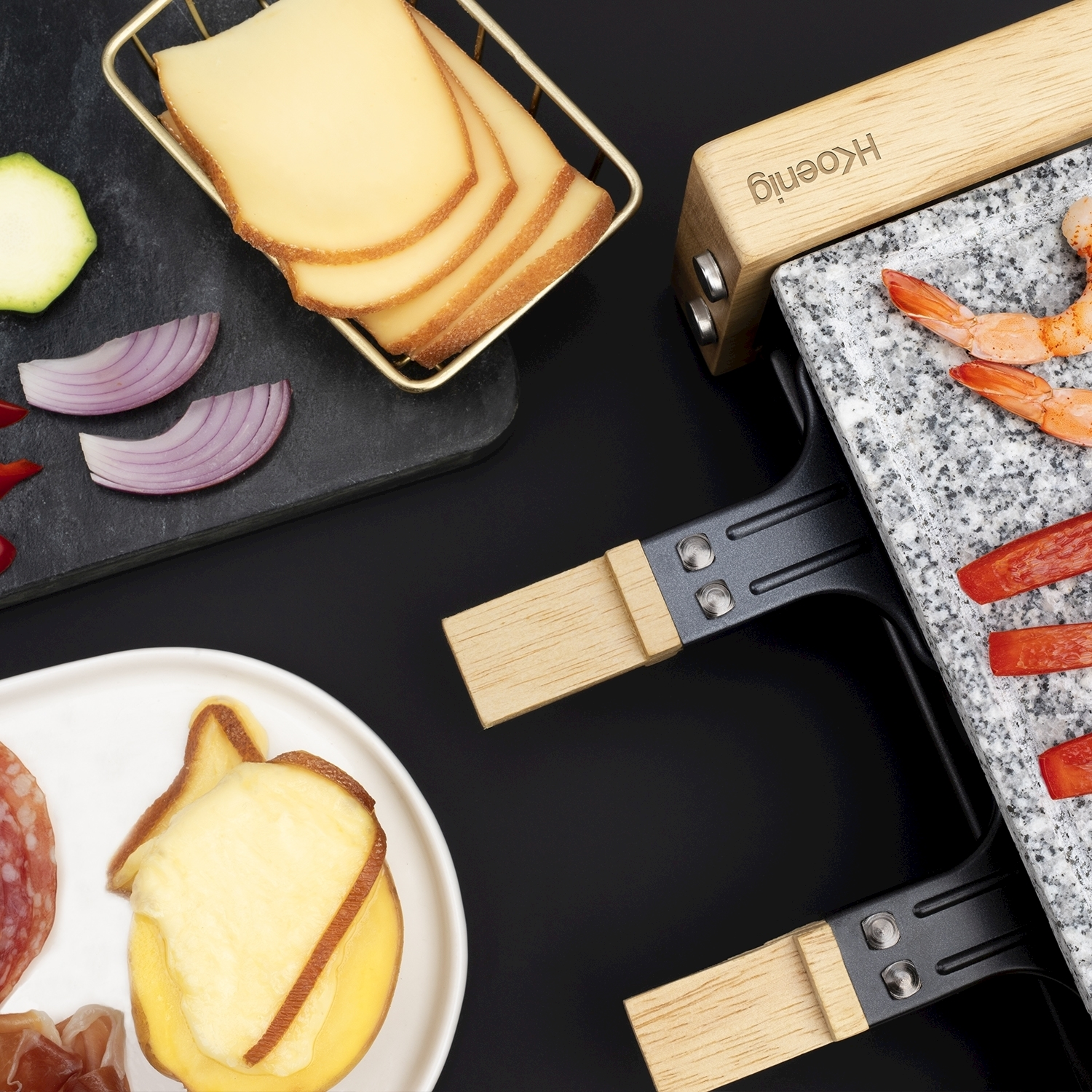 Raclette con formaggio, gamberi, peperoni rossi e cipolle su una superficie nera. Un piatto con salame e patate.
