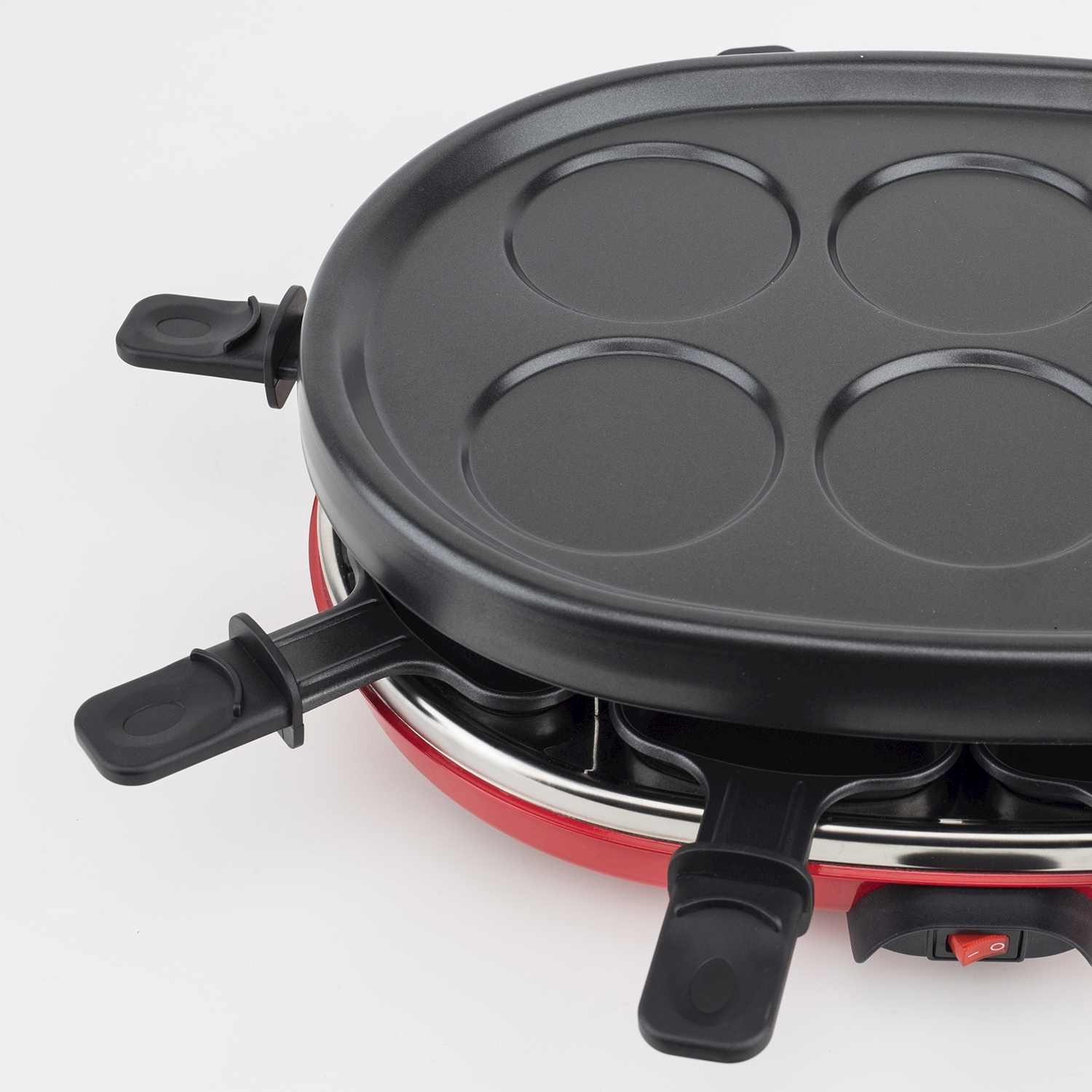 Una griglia per raclette rossa e nera. La griglia ha una parte superiore nera con rientranze circolari e maniglie nere. Una base rossa e un interruttore.