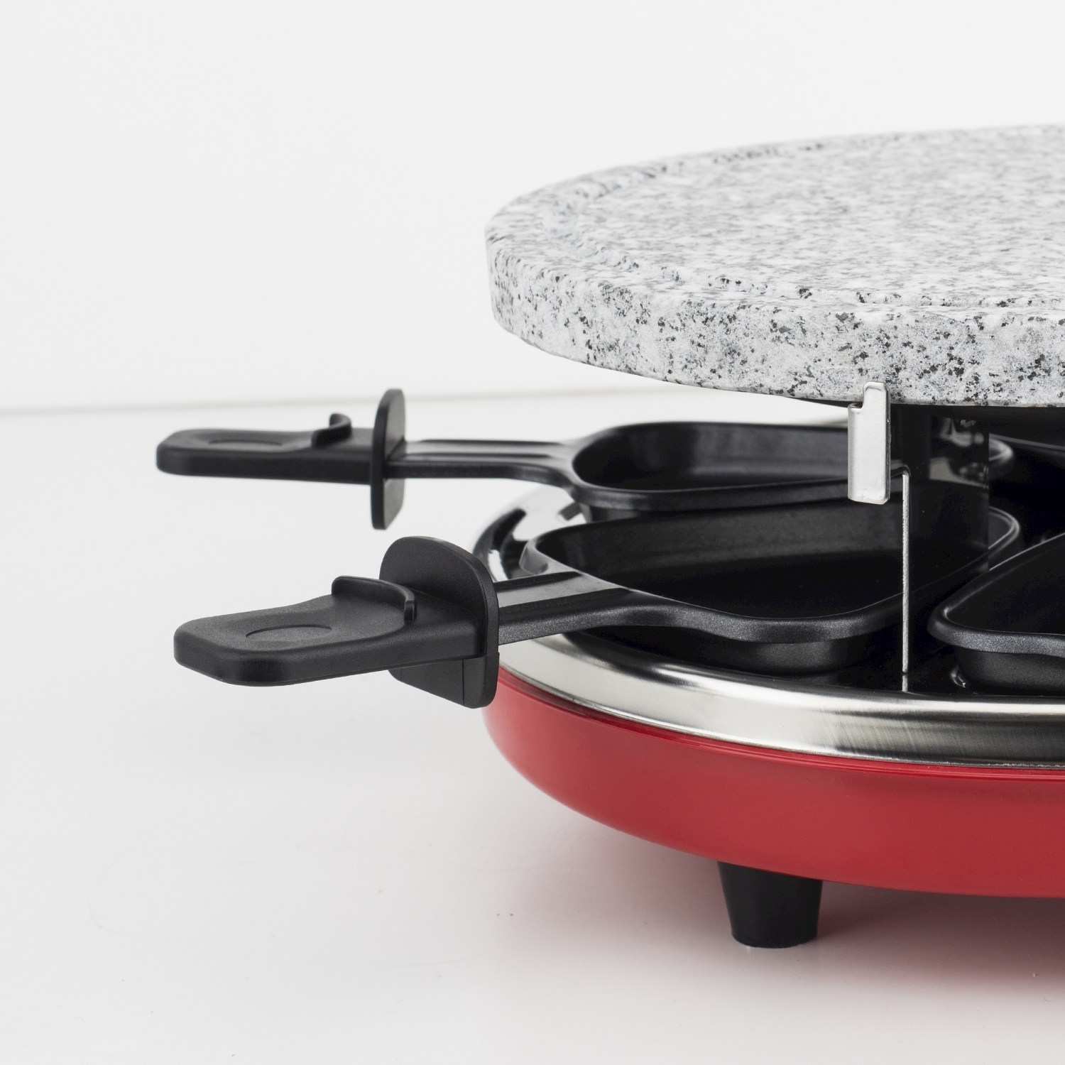 Un primo piano di una griglia per raclette rossa con manici neri e un piano in pietra. La griglia è su una superficie bianca.