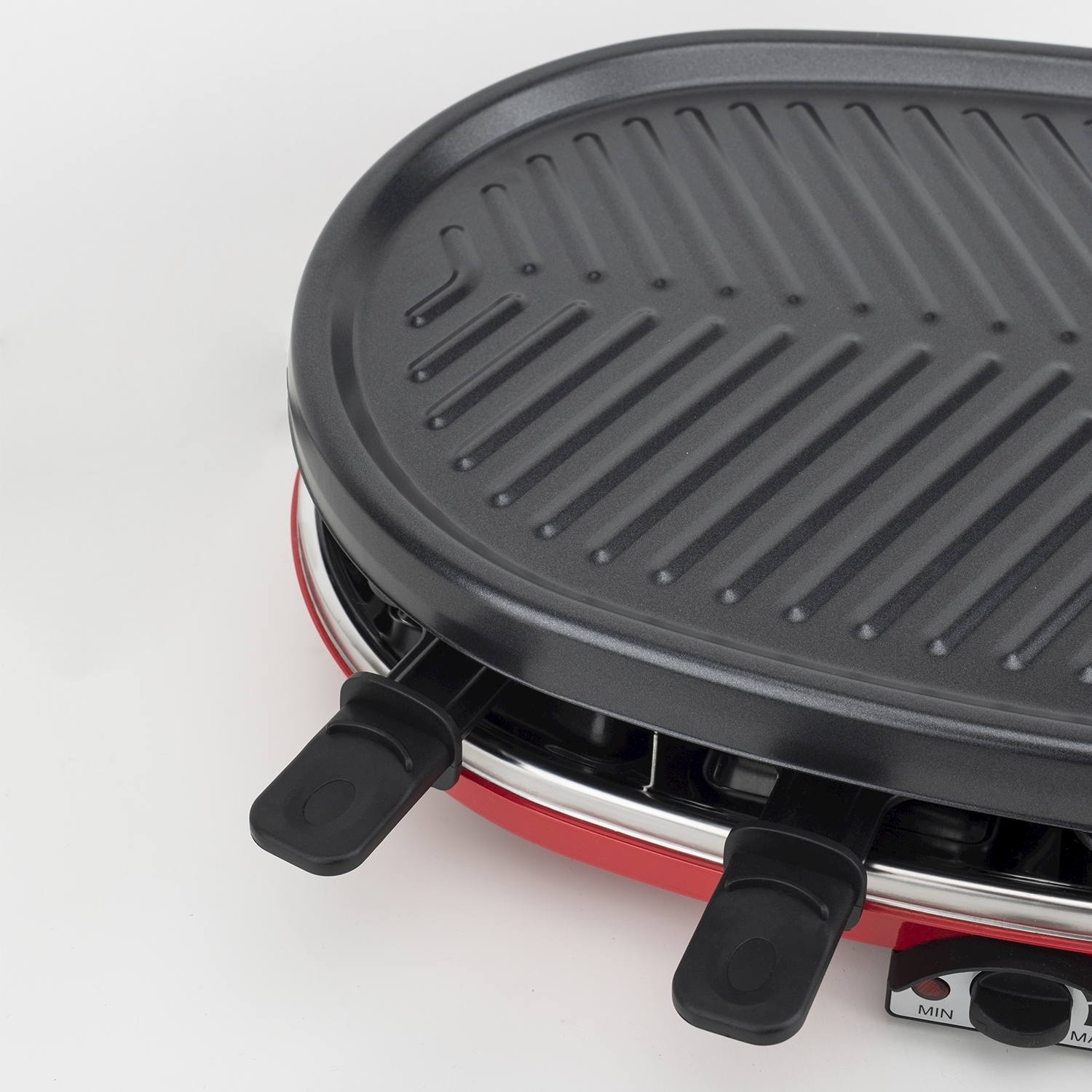 Primo piano di una griglia per raclette. Ha una parte superiore della griglia nera con creste e una base rossa. Sono visibili due maniglie nere e quadranti di controllo.