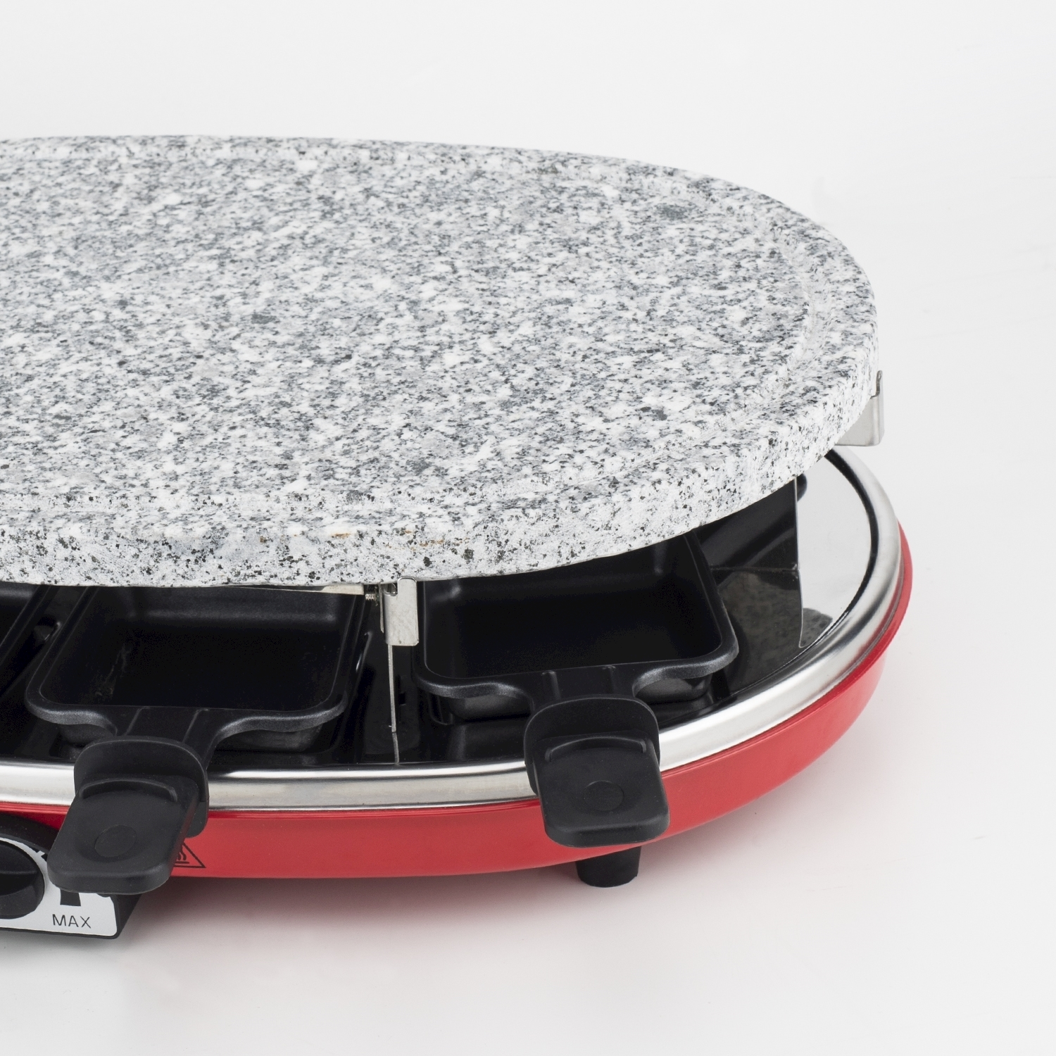 Una griglia per raclette rossa con piano in granito. Ha padelle e manici neri. La griglia è su sfondo bianco.