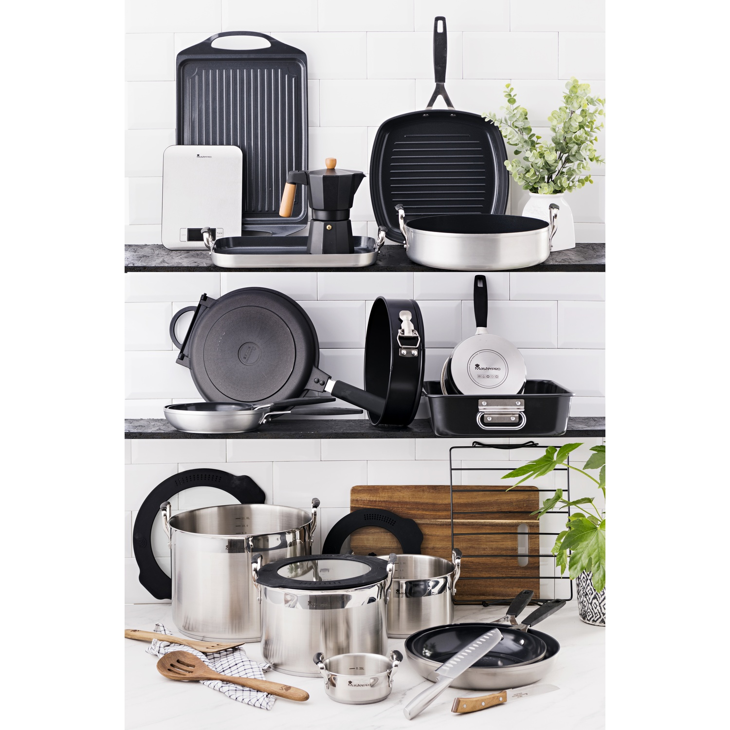 Vari utensili e pentole da cucina esposti su scaffali. Include pentole, padelle, una bilancia e una caffettiera. Una pianta sullo sfondo.