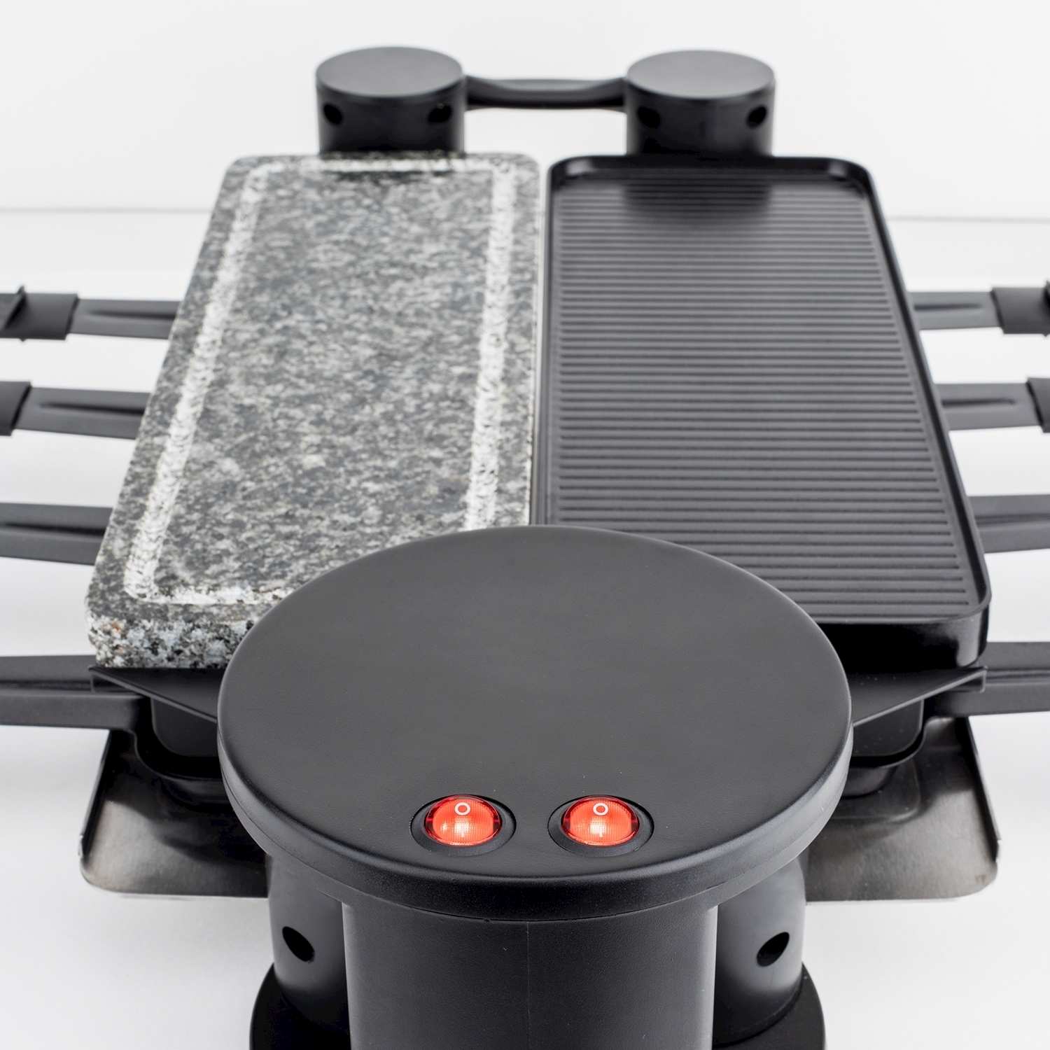 Griglia per raclette con due superfici di cottura: pietra e metallo scanalato. Base nera con spie rosse, su sfondo bianco.