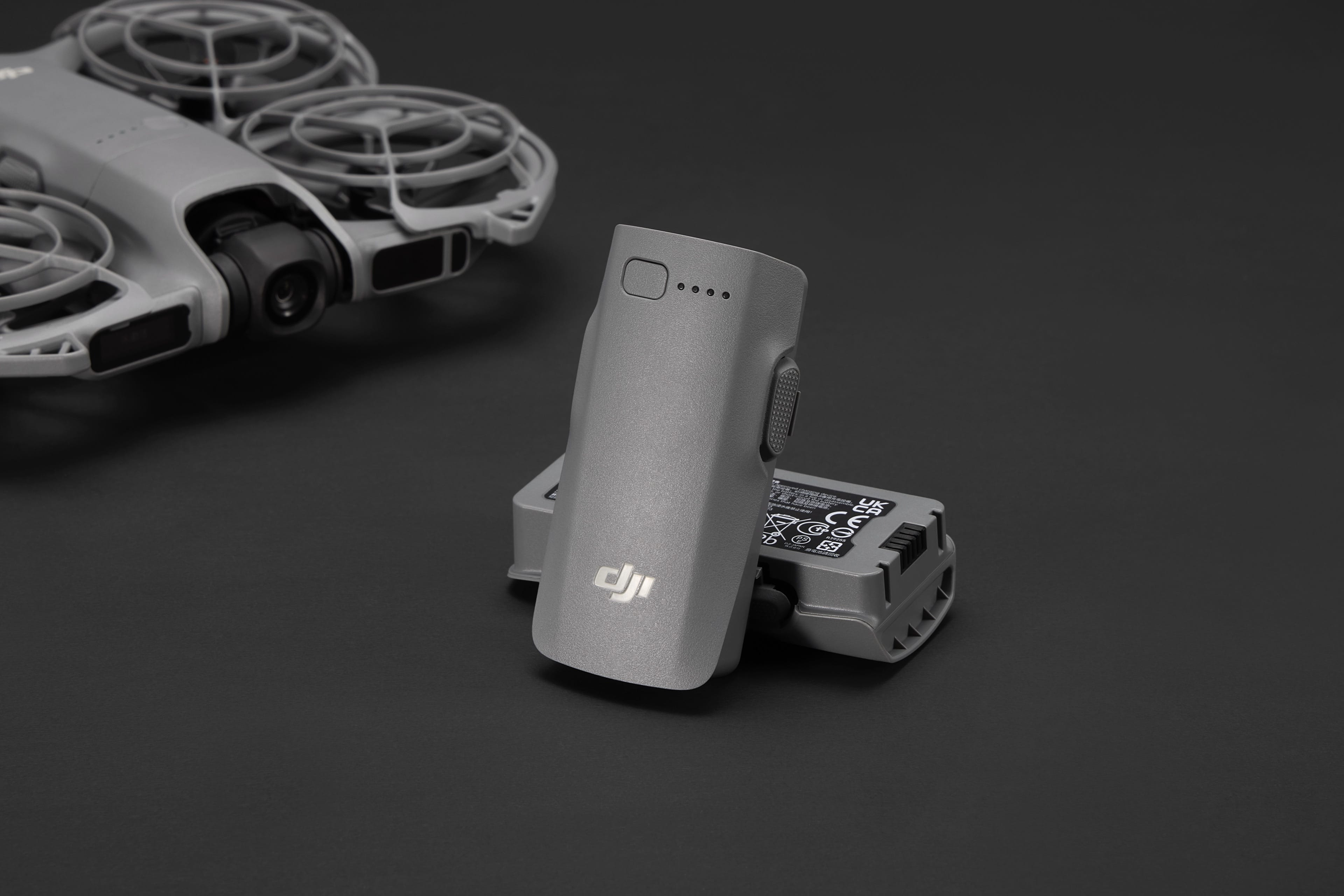 Un drone gris et son chargeur de batterie sur une surface noire. Le chargeur est au-dessus de la batterie.