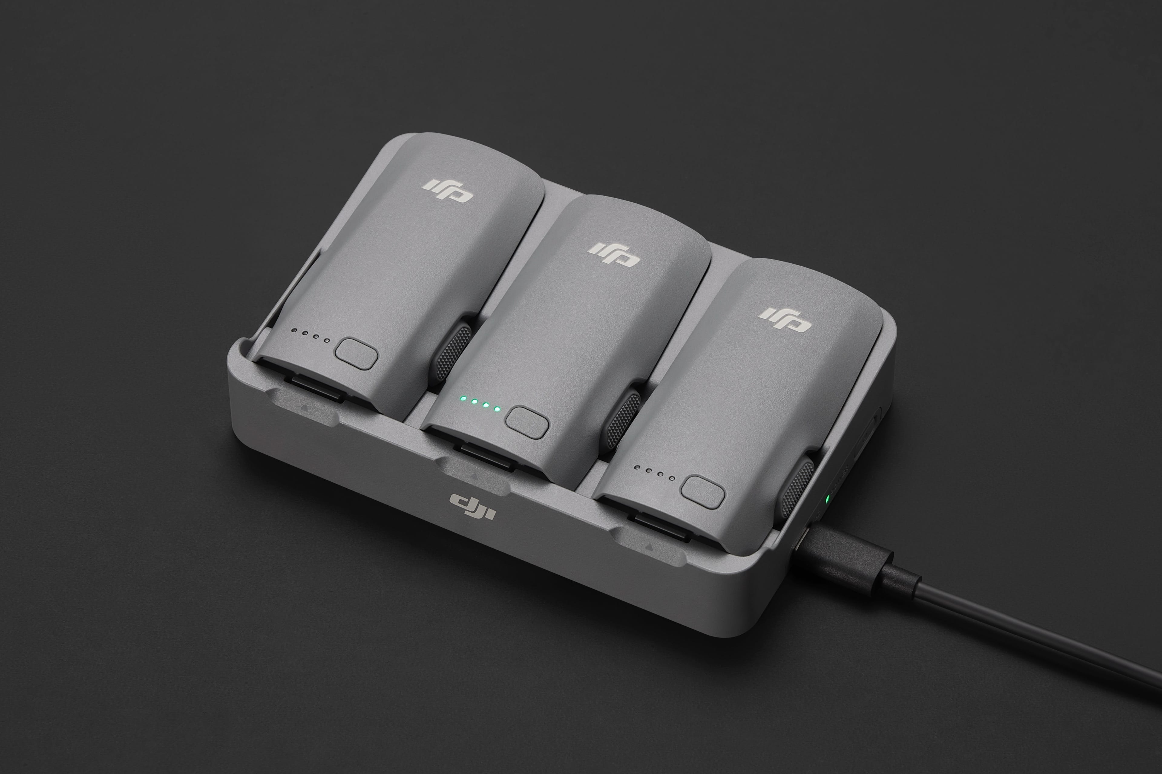 Trois batteries de drone grises dans une station de charge, reliées par un câble noir, sur une surface gris foncé.