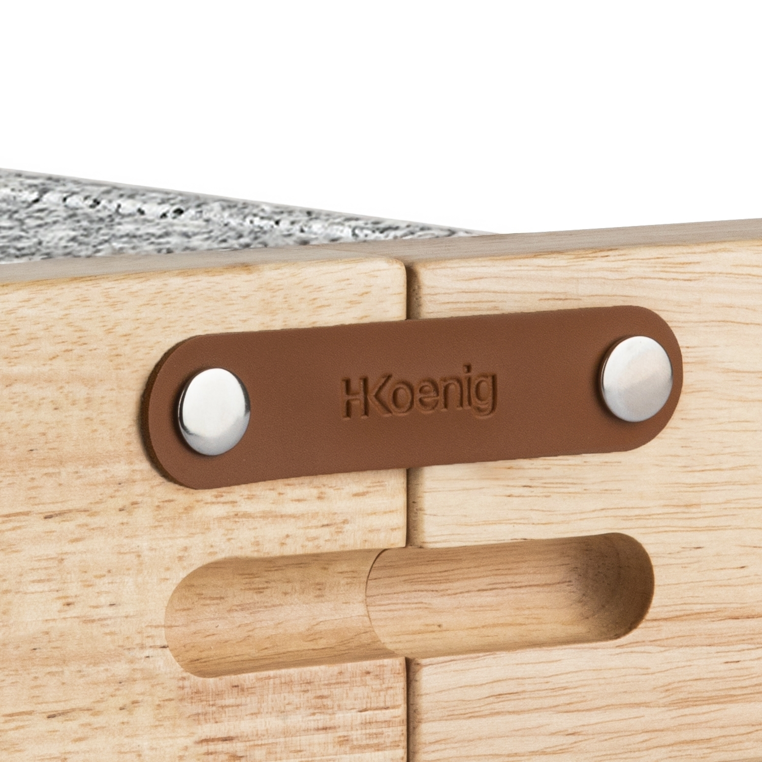 Dettaglio tavolo pieghevole in legno. Targhetta in pelle marrone con borchie metalliche e 'HKoenig' in rilievo. Manico in legno. Venatura chiara.