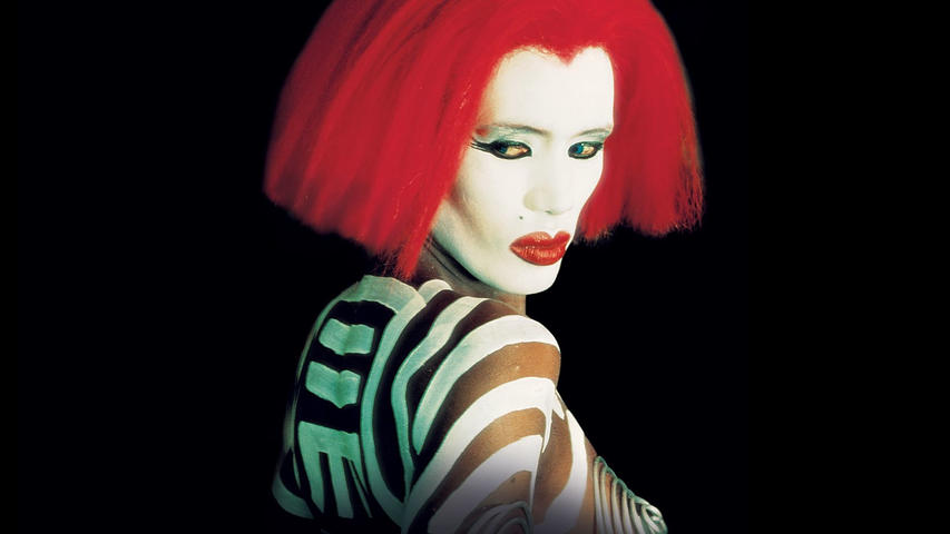 Eine Frau mit rotem Haar und weißer Gesichtsbemalung. Sie hat Zebrastreifen auf der Schulter, rote Lippen und dunkles Augen-Make-up, vor schwarzem Hintergrund.