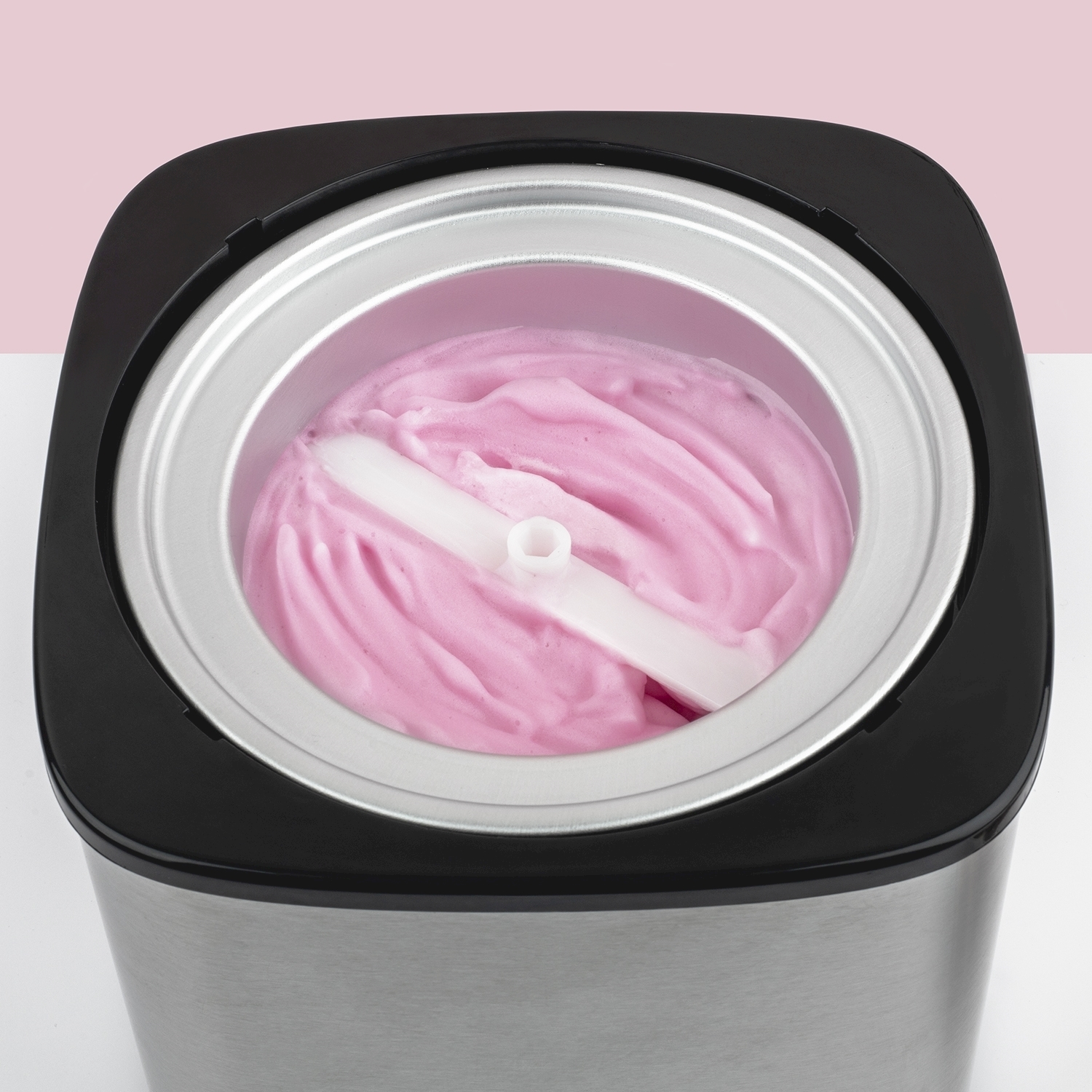 Una gelatiera con gelato rosa all'interno. Una paletta di plastica bianca al centro. Lo sfondo è rosa e bianco.