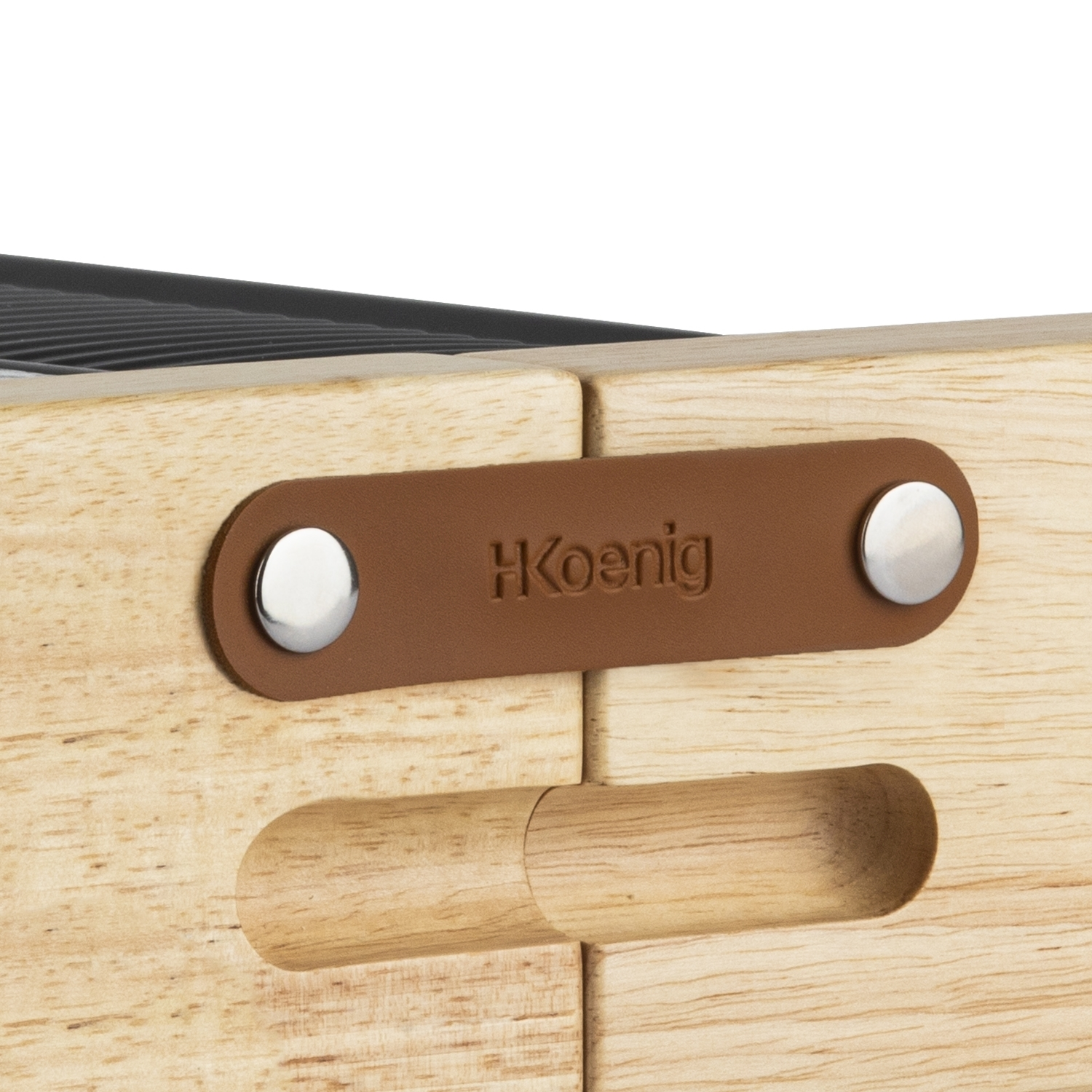 Primo piano di una scatola di legno. Un'etichetta in pelle marrone con 'H Koenig' è attaccata. Rivetti argentati e una maniglia in legno sono visibili.