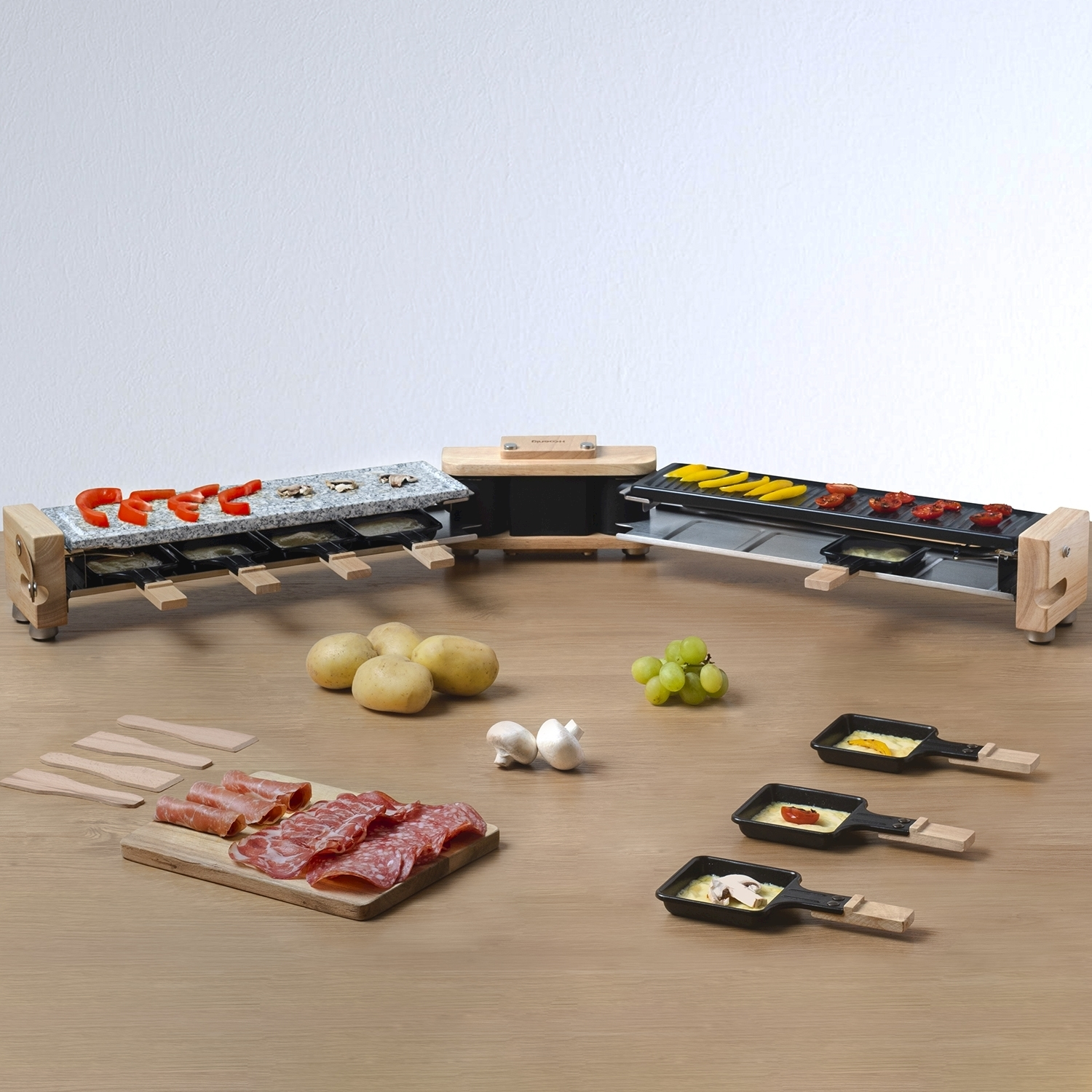 Griglia per raclette con verdure e carne, con patate, uva e funghi su un tavolo di legno.