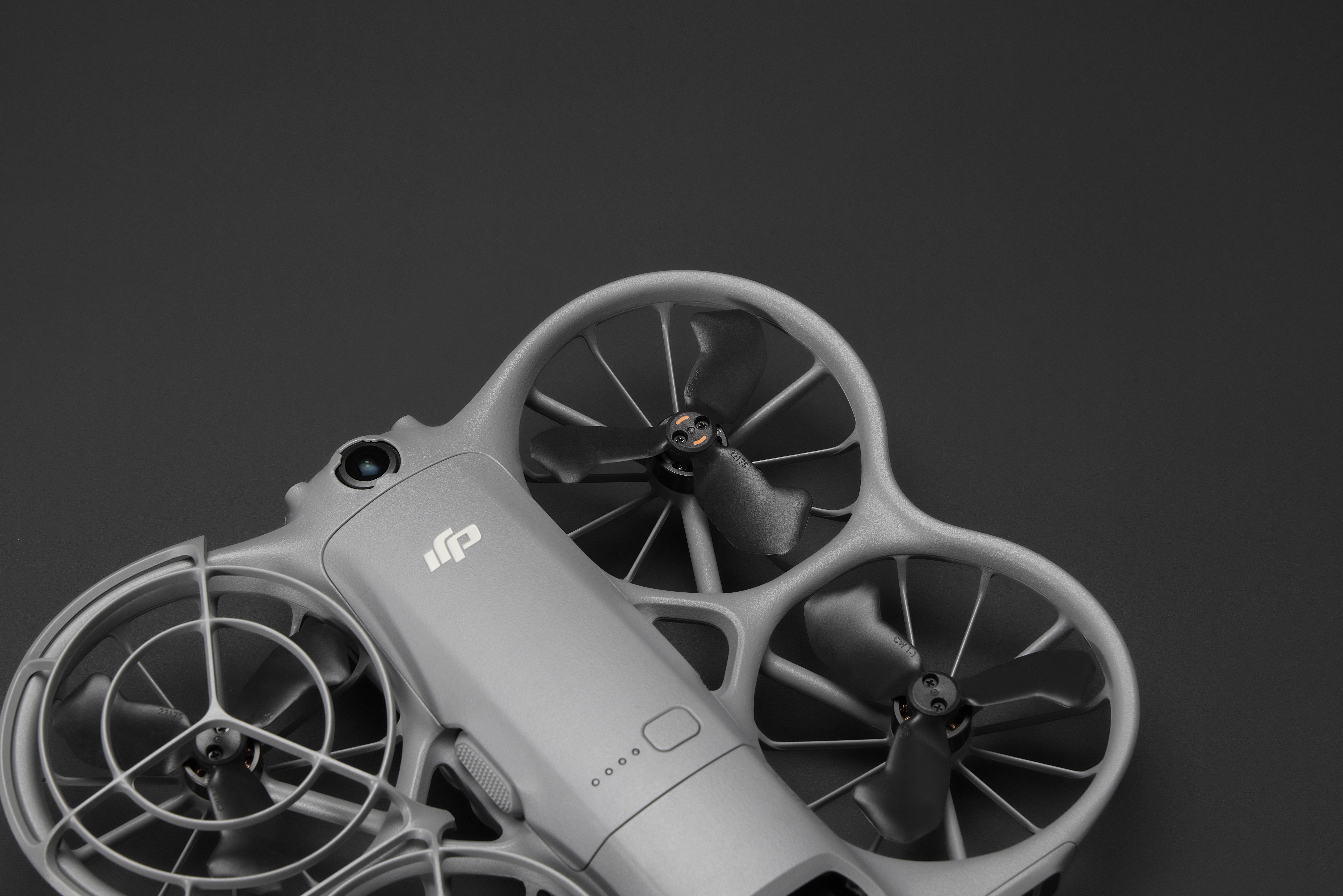 Un drone gris avec des hélices est posé sur une surface noire. Le drone a une caméra et le logo DJI. Le fond est gris foncé.