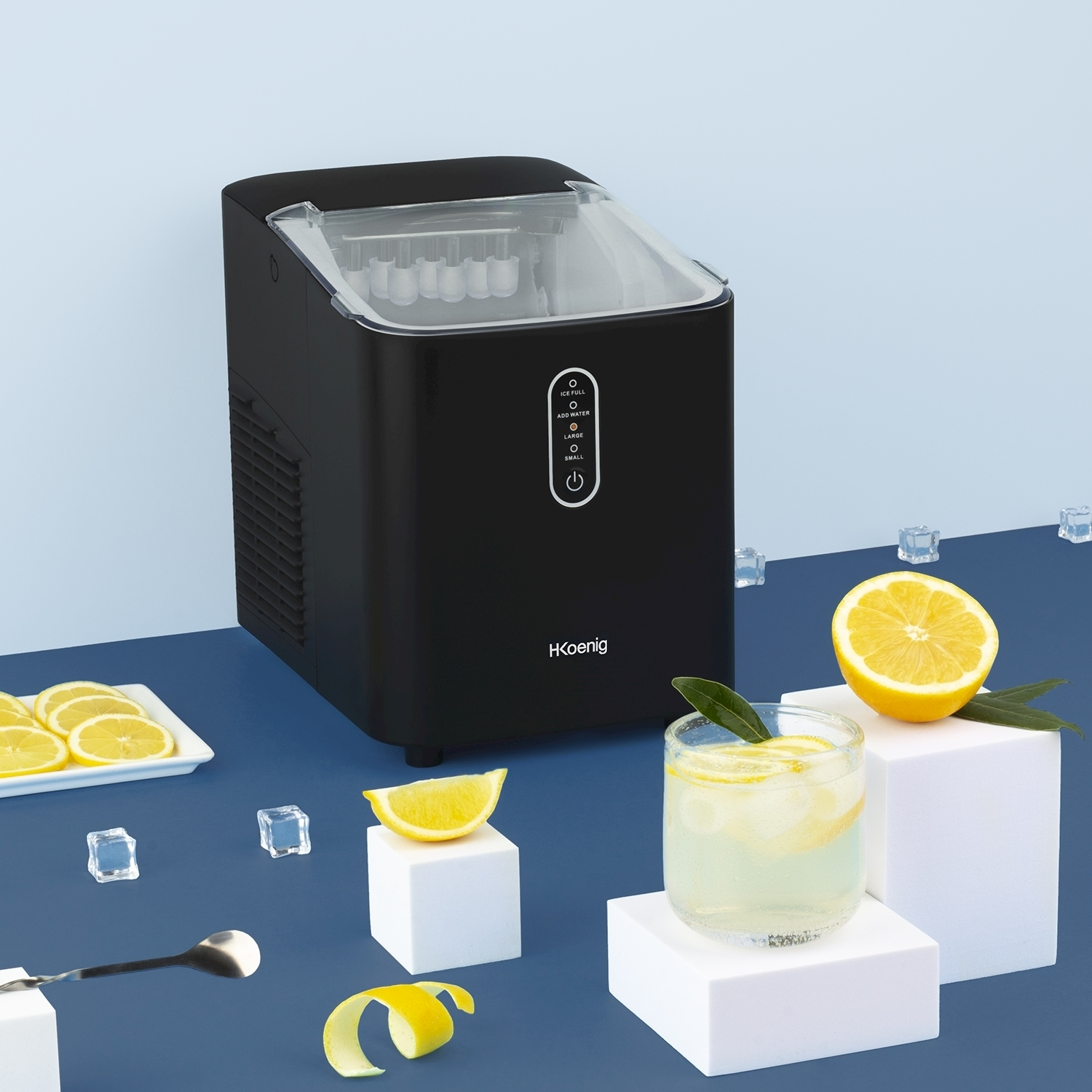 Fabbricatore di ghiaccio nero, bicchiere di limonata, fette di limone, cubetti di ghiaccio e mezzo limone su superficie blu. Cubi bianchi.
