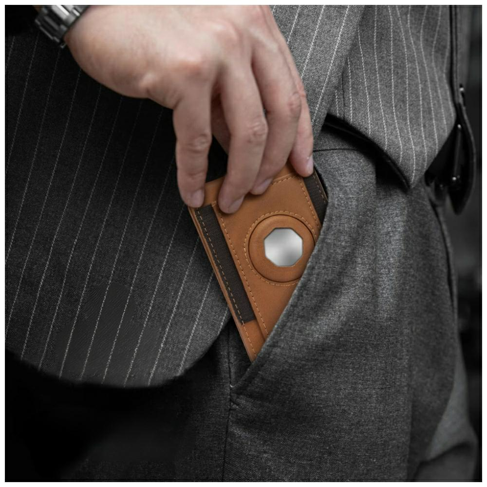 Mężczyzna w szarym garniturze wkłada brązowy portfel ze srebrnym kółkiem do kieszeni.