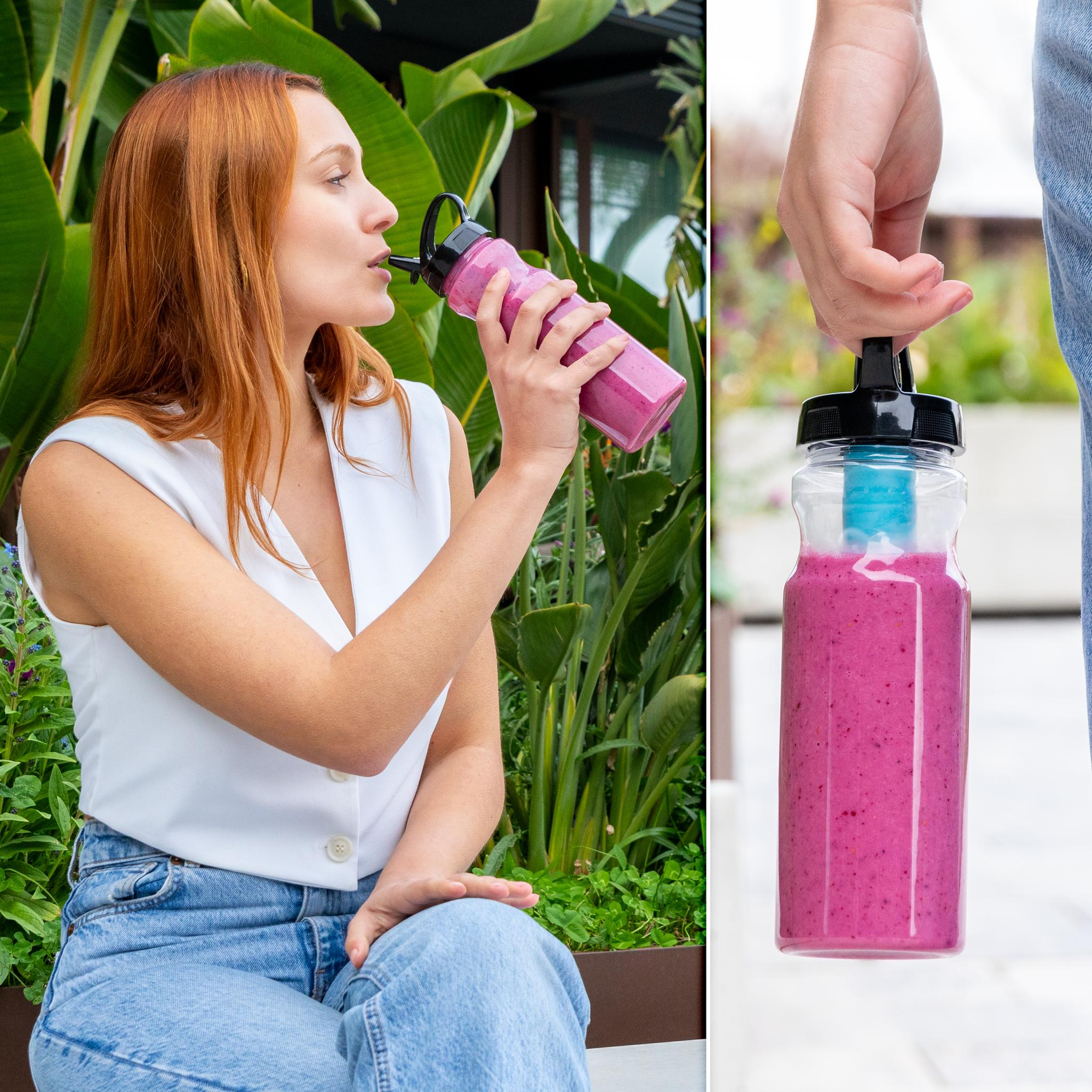 Mujer bebiendo un batido rosa de una botella. Está sentada afuera con exuberantes plantas verdes al fondo.
