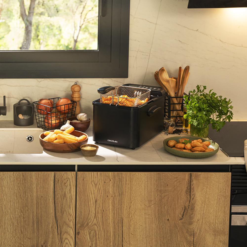 Escena de cocina con freidora, patatas fritas, cebollas, ajo y perejil. Armarios de madera y una ventana al fondo.
