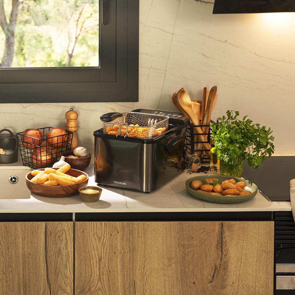 Una escena de cocina con una freidora, comida y utensilios. Los gabinetes de madera están en primer plano. Una ventana está al fondo.