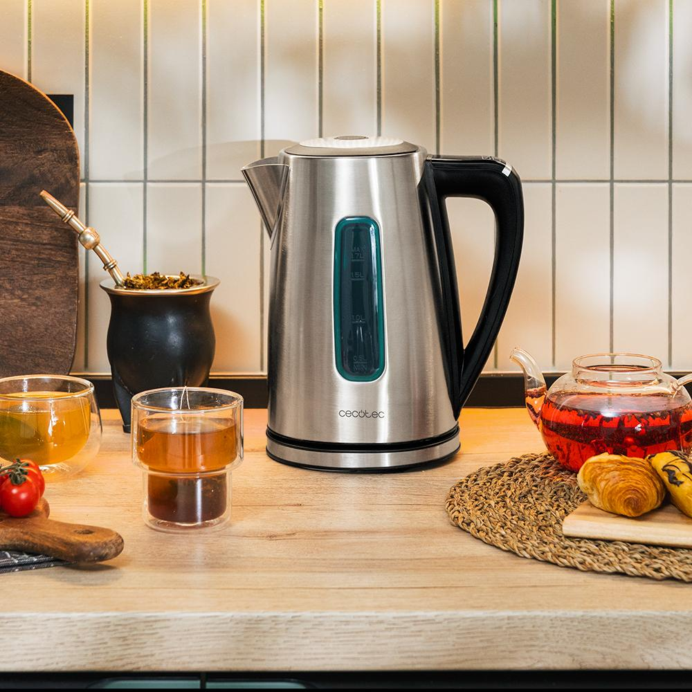 Una tetera de acero inoxidable, vasos de vidrio y una tetera con té sobre una superficie de madera. También hay una taza de mate y cruasanes.