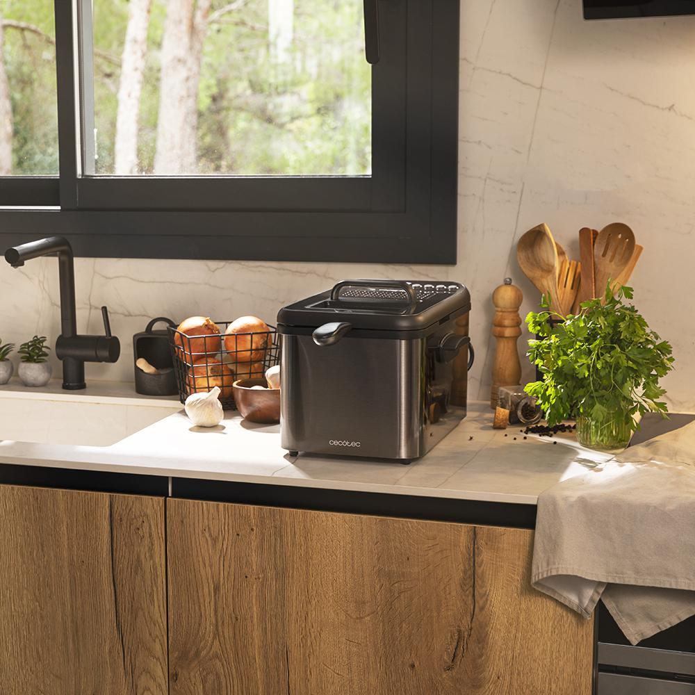 Una escena de cocina con una freidora, verduras y utensilios. Una ventana muestra una vista de árboles.