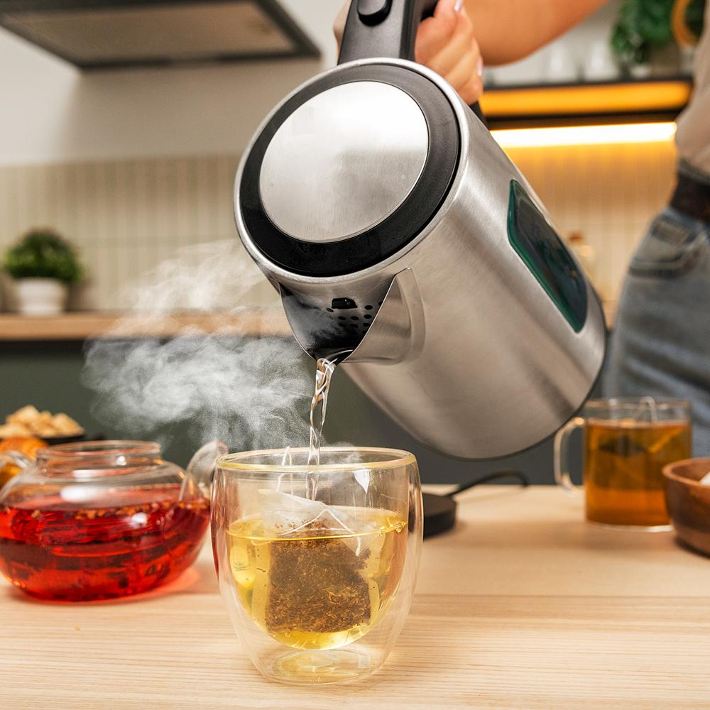 Una persona vierte agua caliente de una tetera en un vaso de té. Una bolsita de té está dentro del vaso. Se ven otros vasos de té.