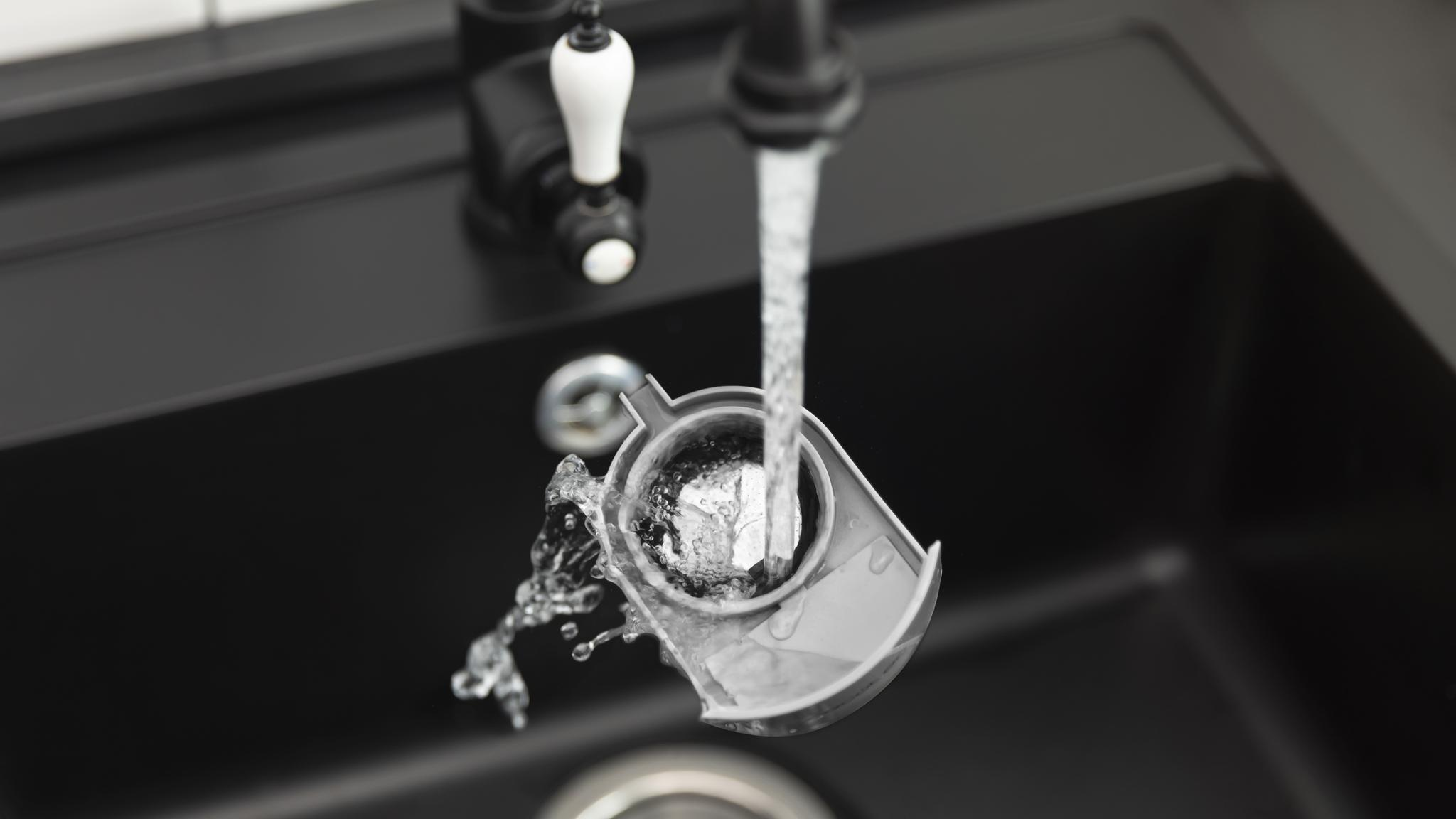 El agua fluye de un grifo a un filtro gris. Un fregadero negro está en el fondo. El grifo tiene un mango blanco.