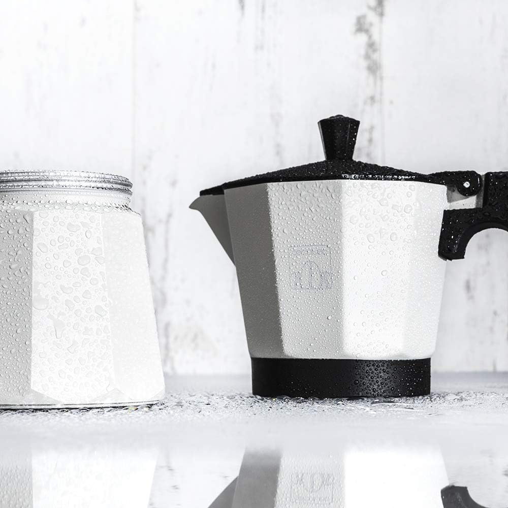 Una cafetera blanca y un tarro con gotas de agua sobre una superficie y fondo blancos.