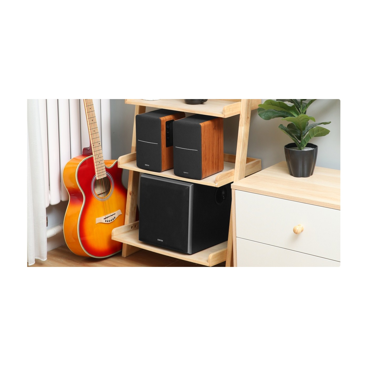Chitarra acustica accanto a una mensola di legno con altoparlanti e un subwoofer. Sono presenti anche una pianta e un mobile bianco.