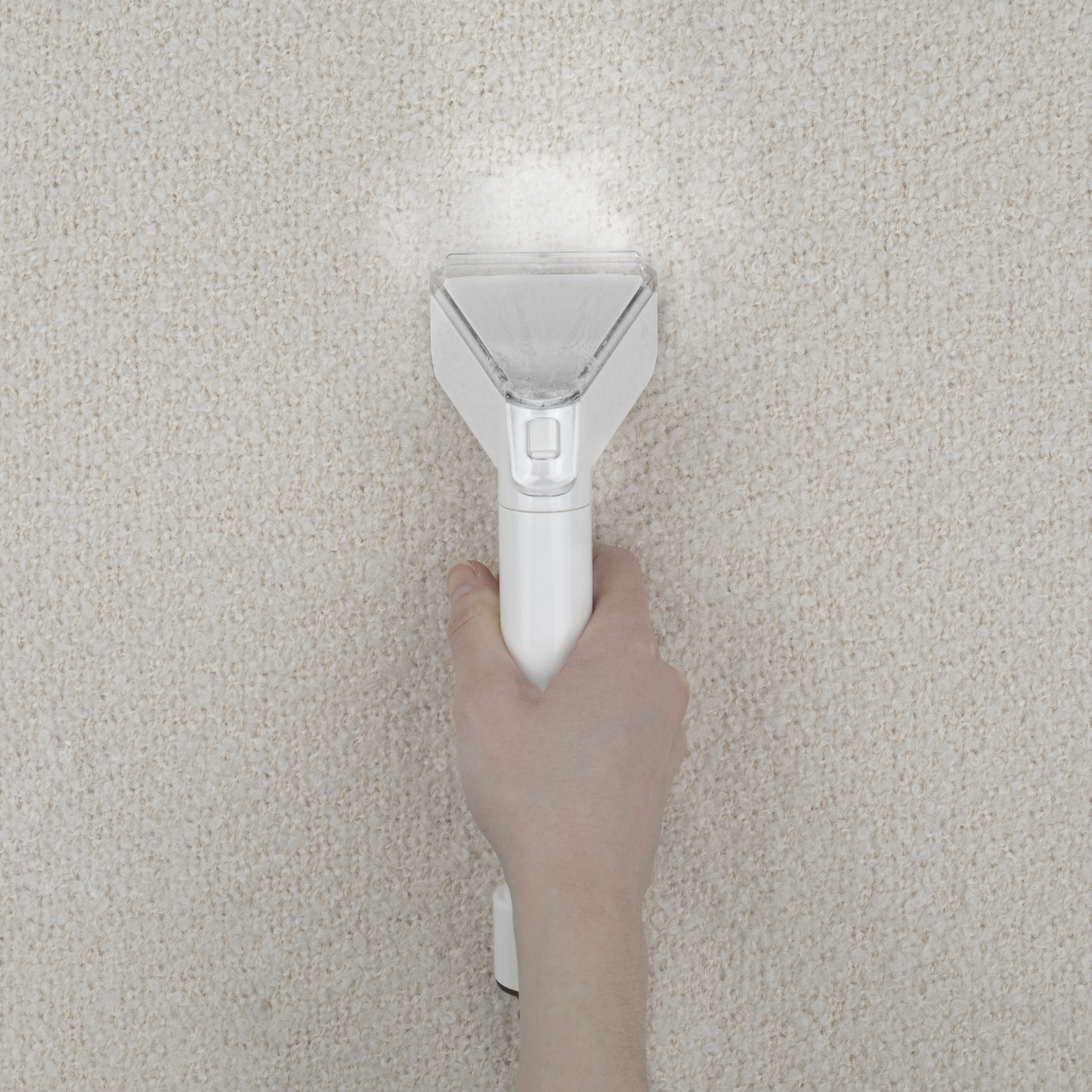 Una mano tiene un pulitore per tappeti bianco sopra un tappeto beige. Il pulitore è acceso e sta spruzzando il tappeto.