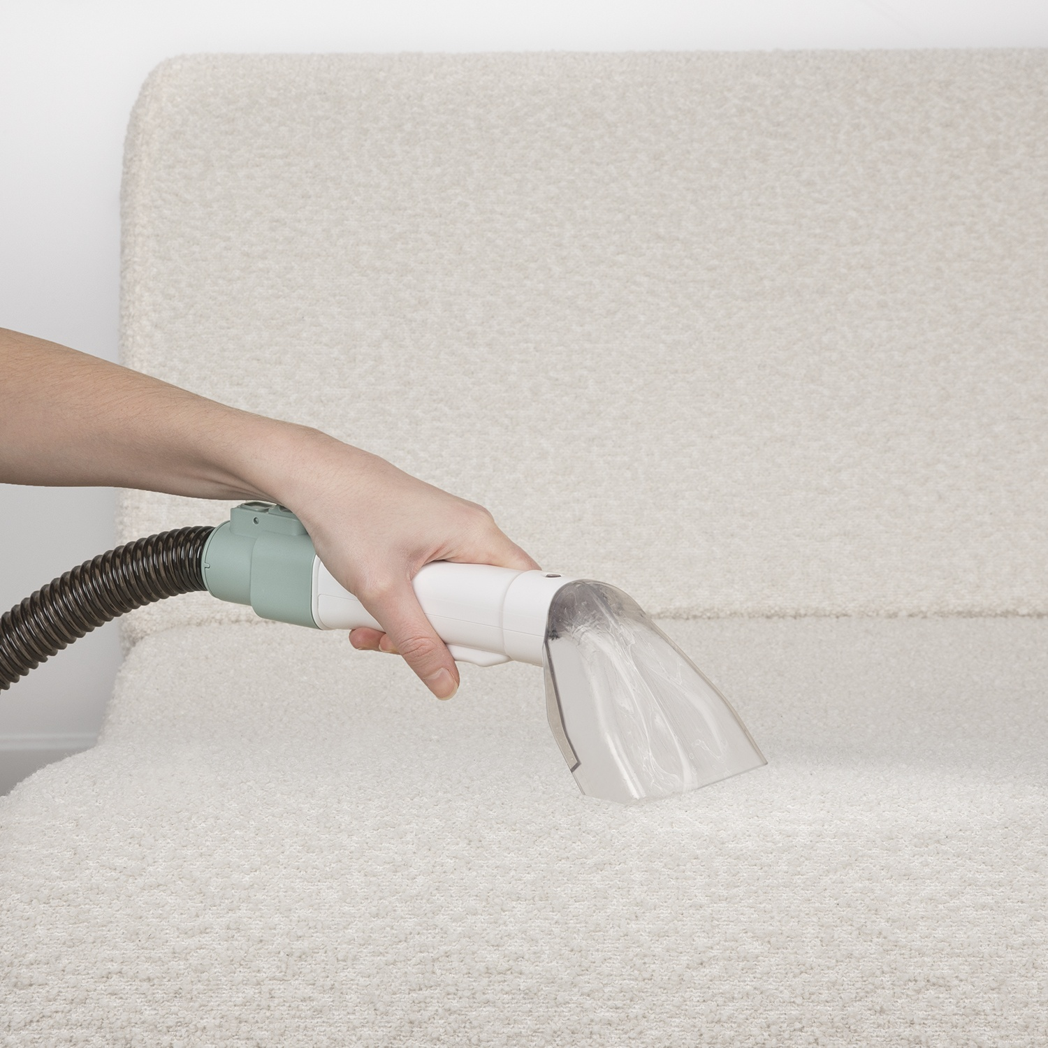 Una persona pulisce un tappeto di colore chiaro con un pulitore per tappeti portatile. Il pulitore è bianco e verde.
