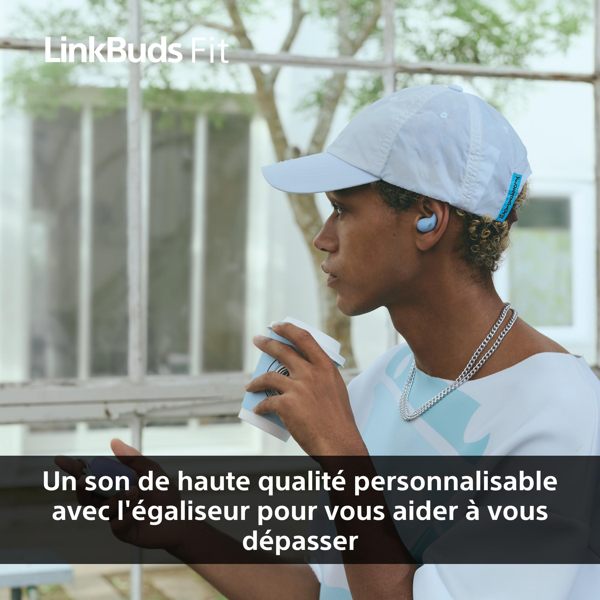 Une personne portant des écouteurs et une casquette, tenant une tasse de café. L'arrière-plan a une fenêtre et des arbres.