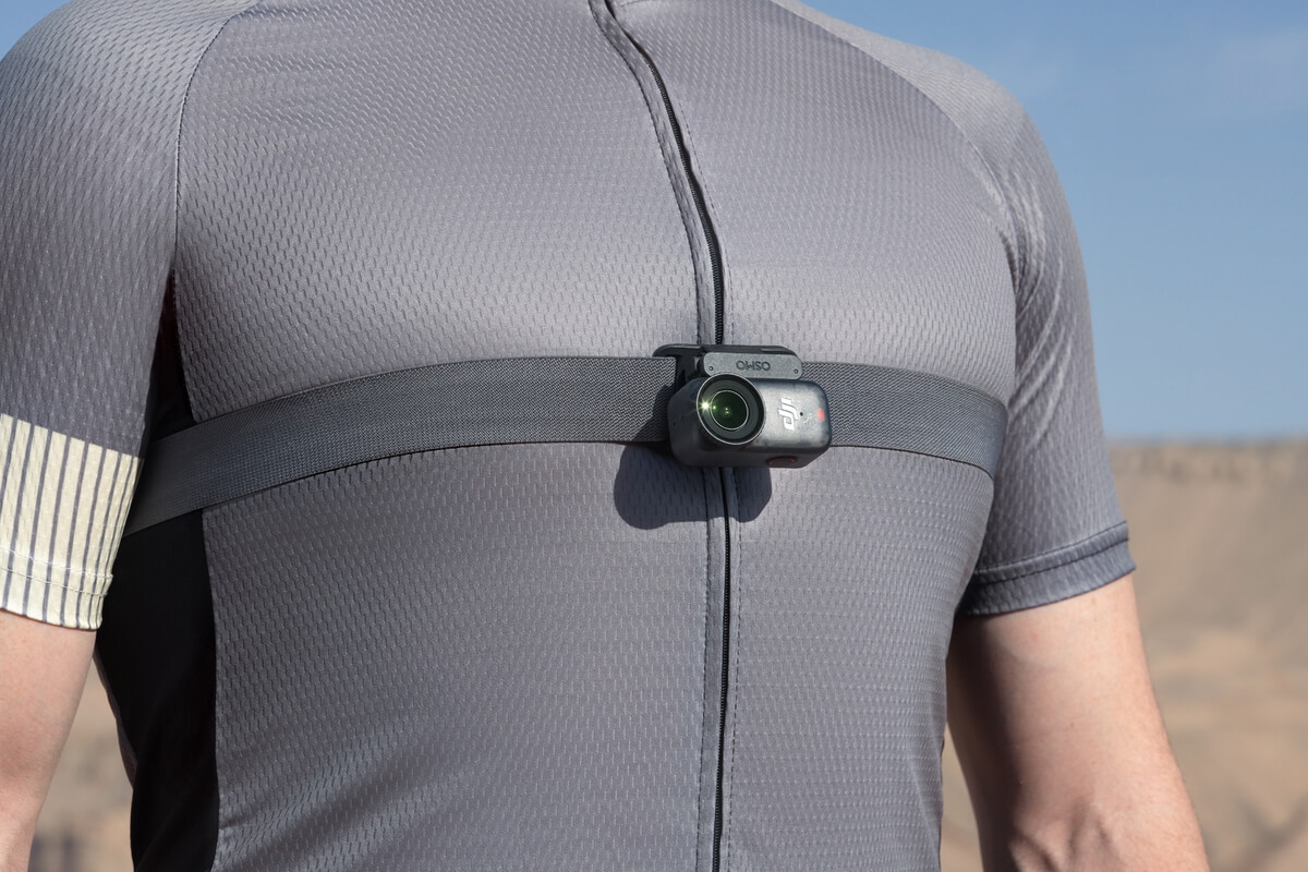 Eine Person trägt ein graues Radtrikot mit einer Brustkamera. Die Kamera ist an einem Gurt über der Brust befestigt.