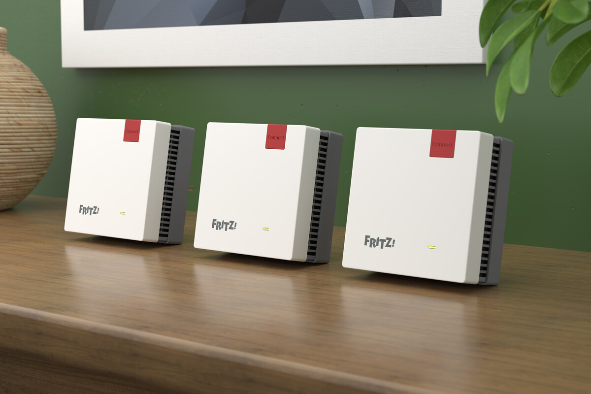 Trois routeurs blancs FRITZ! avec étiquettes rouges 'Connect', sur une surface en bois, fond de mur vert et une plante.
