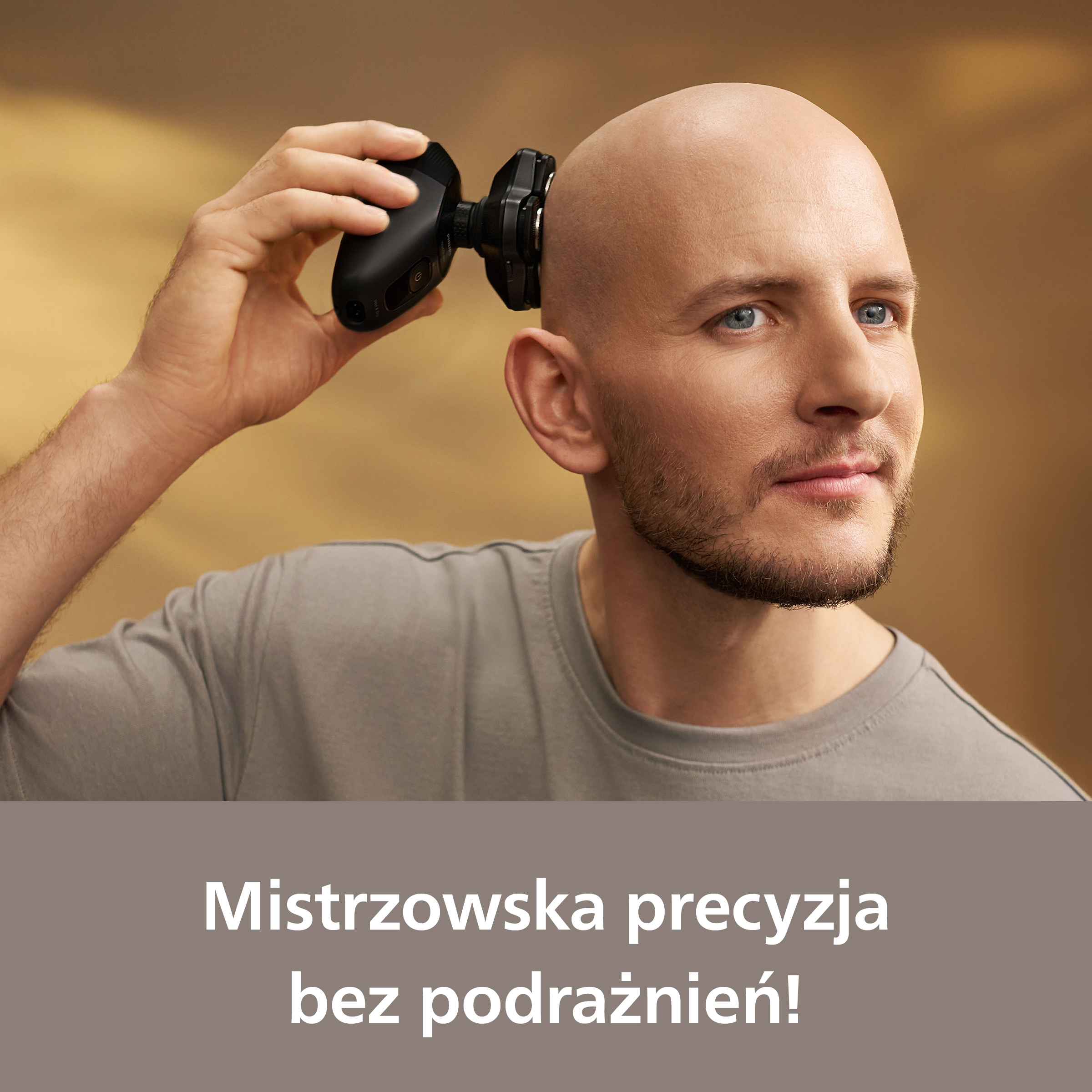 Mężczyzna goli głowę golarką elektryczną. Ma niebieskie oczy i jasną brodę. Tło jest rozmyte.