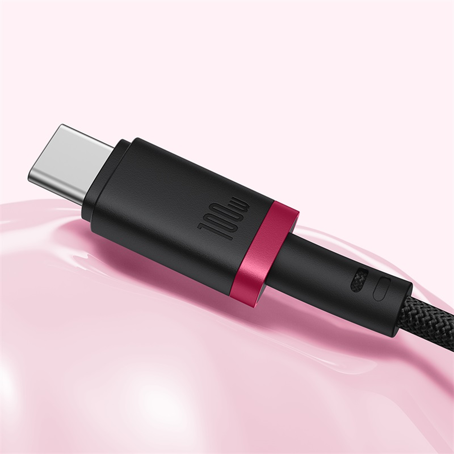 Primer plano de un cable USB-C negro con un acento rojo, etiquetado 100w, contra un fondo rosa.