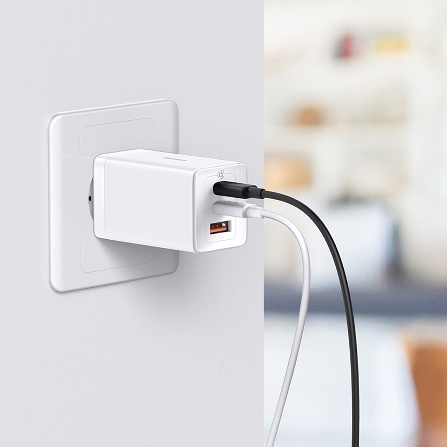 Un adaptador de corriente blanco enchufado a una toma de corriente. Cables de carga negros y blancos conectados. Fondo borroso.
